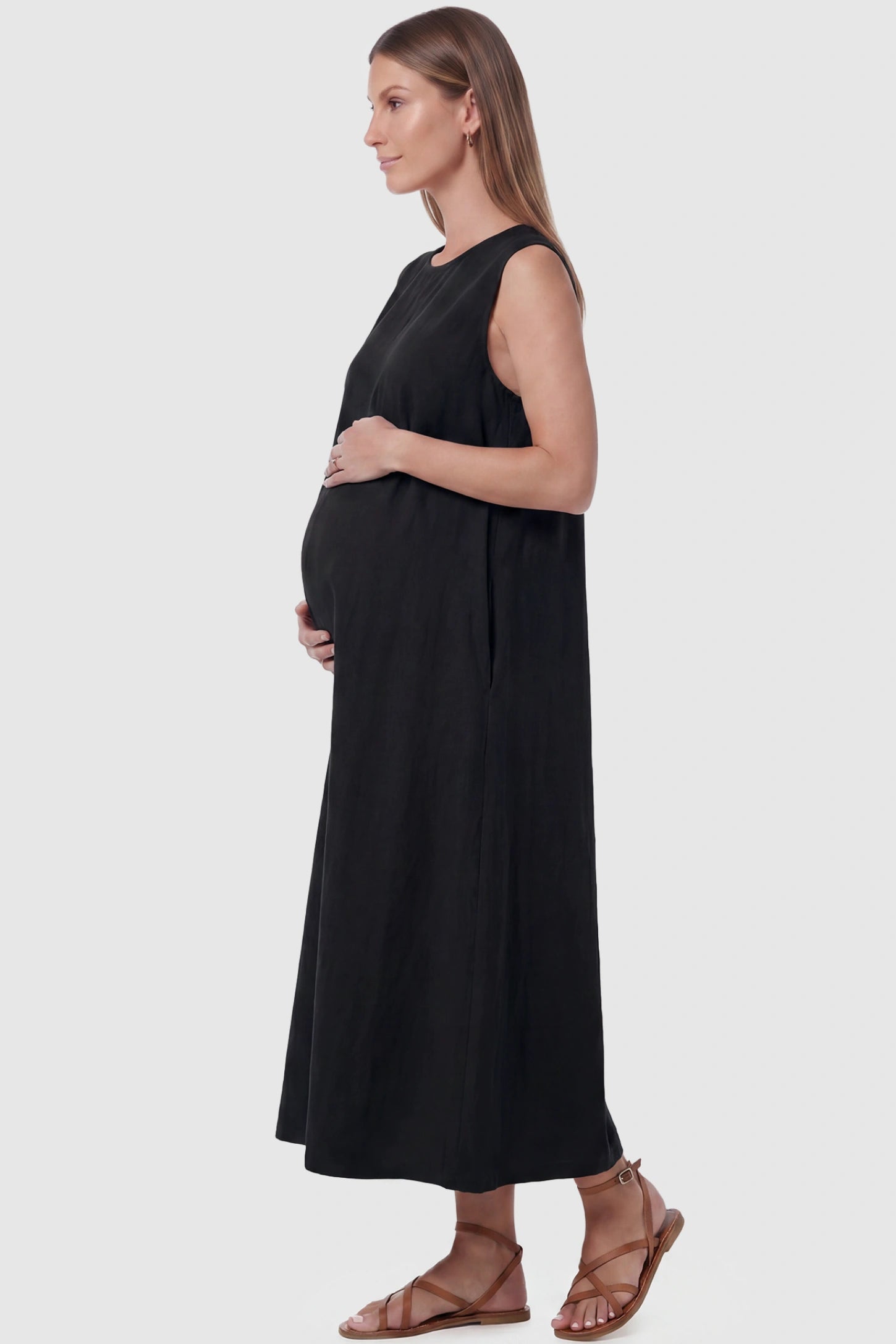 Sleeveless Pocketed Longline Hem Maternity Midi Dress Sleeveless pocketed longline hem maternity midi dress in black with sleeveless design and side pocket, side view on pregnant model