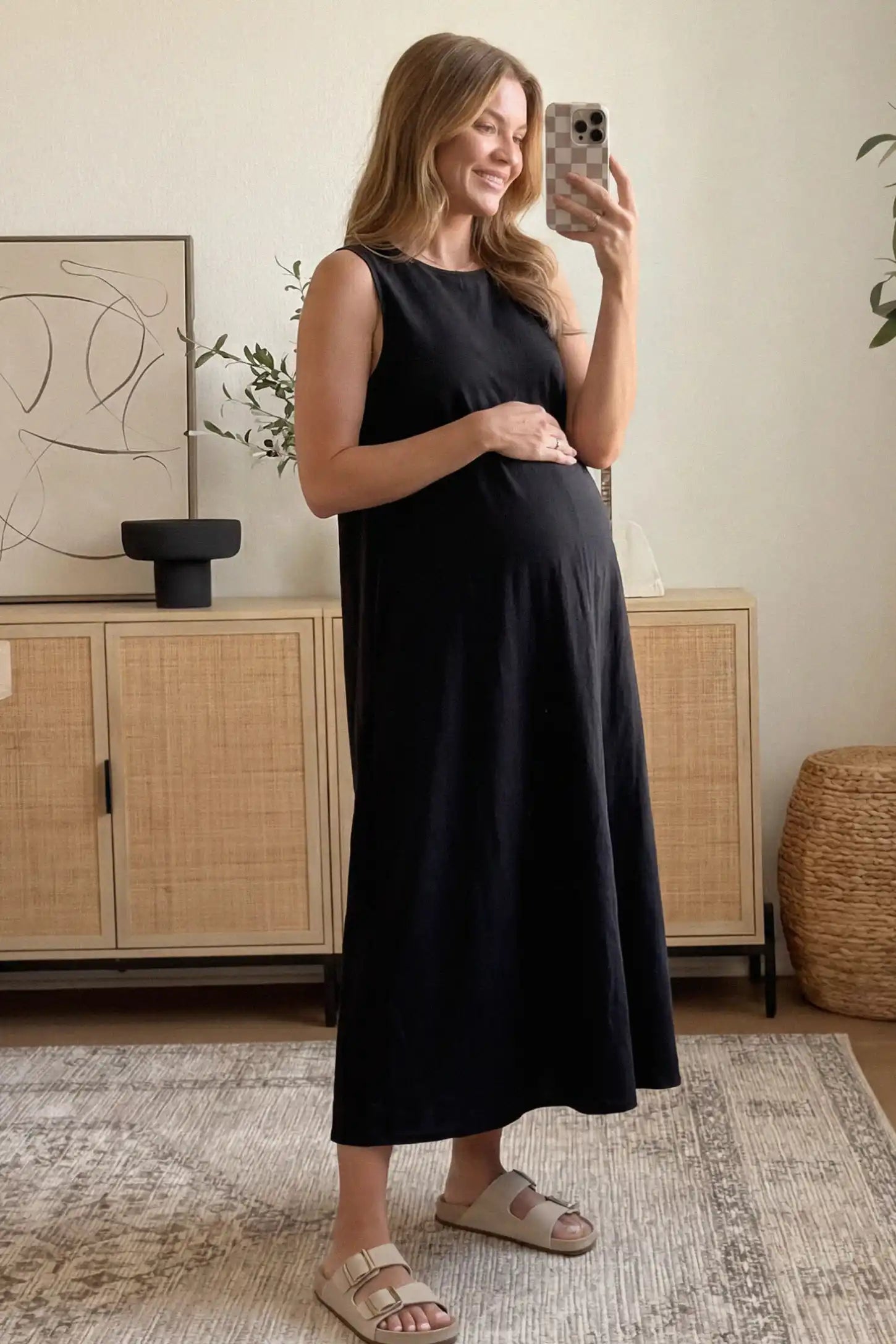 Sleeveless Pocketed Longline Hem Maternity Midi Dress Sleeveless pocketed longline hem maternity midi dress in black with sleeveless design and longline hem, side view on pregnant model