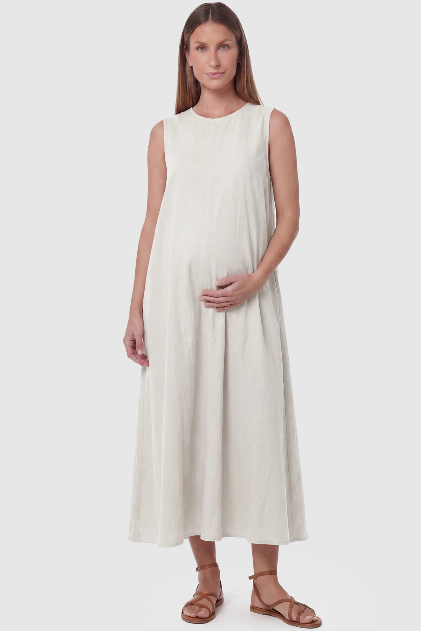 Sleeveless Pocketed Longline Hem Maternity Midi Dress Sleeveless pocketed longline hem maternity midi dress in cream with sleeveless design and longline hem, front view on pregnant model