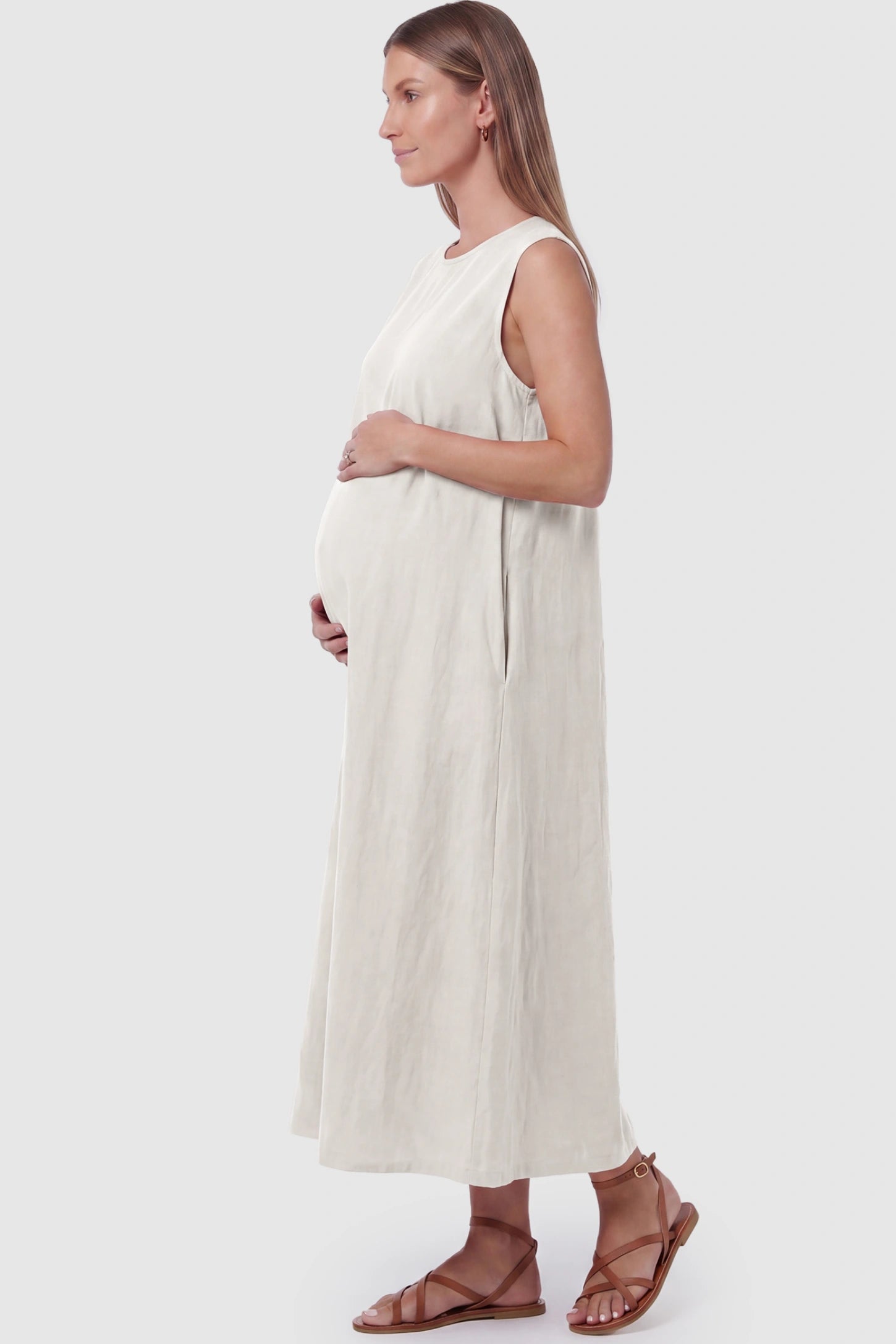 Sleeveless Pocketed Longline Hem Maternity Midi Dress Sleeveless pocketed longline hem maternity midi dress in cream with sleeveless design and side pocket, side view on pregnant model