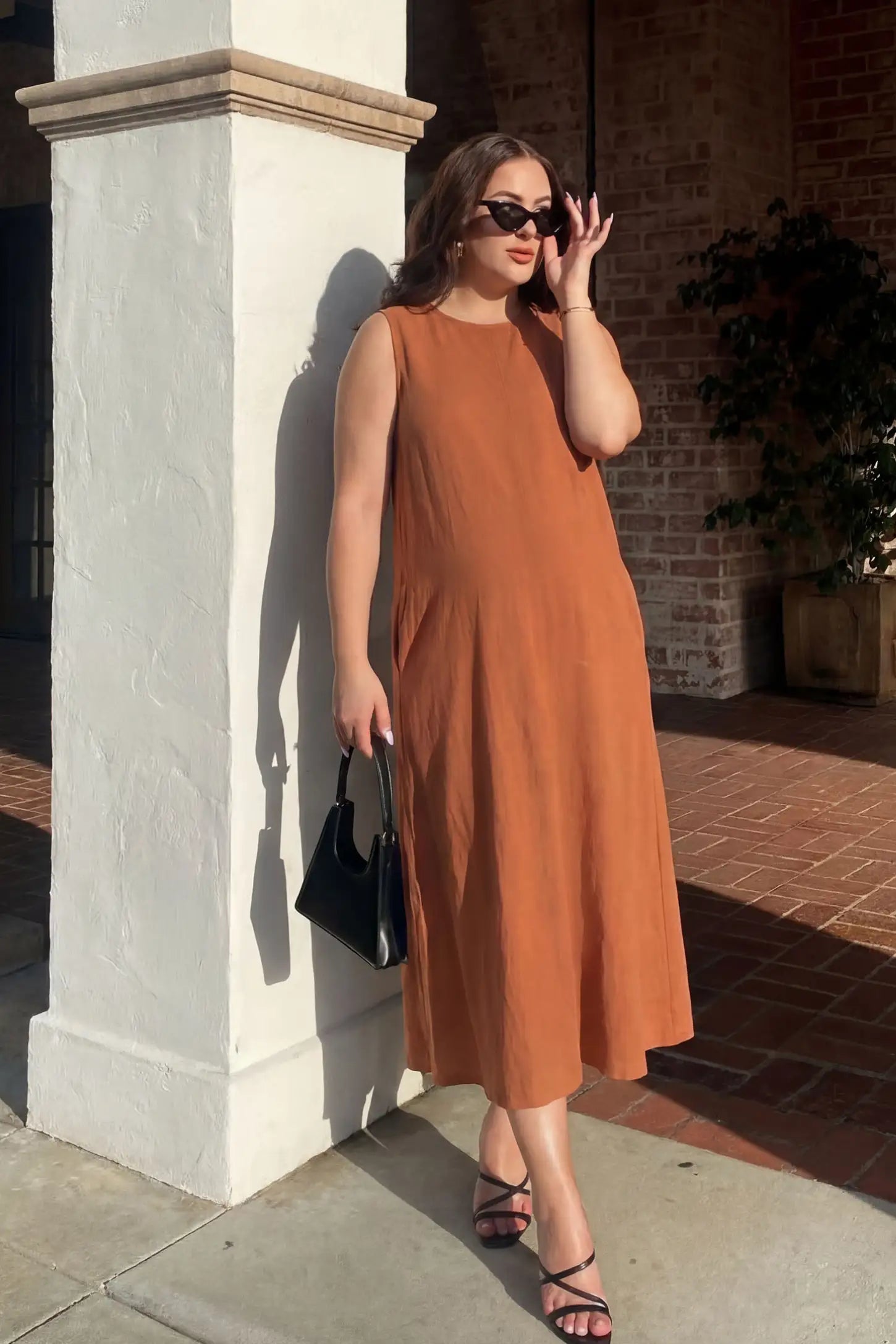 Sleeveless Pocketed Longline Hem Maternity Midi Dress Sleeveless pocketed longline hem maternity midi dress in rust brown with sleeveless design and longline hem, front view on pregnant model