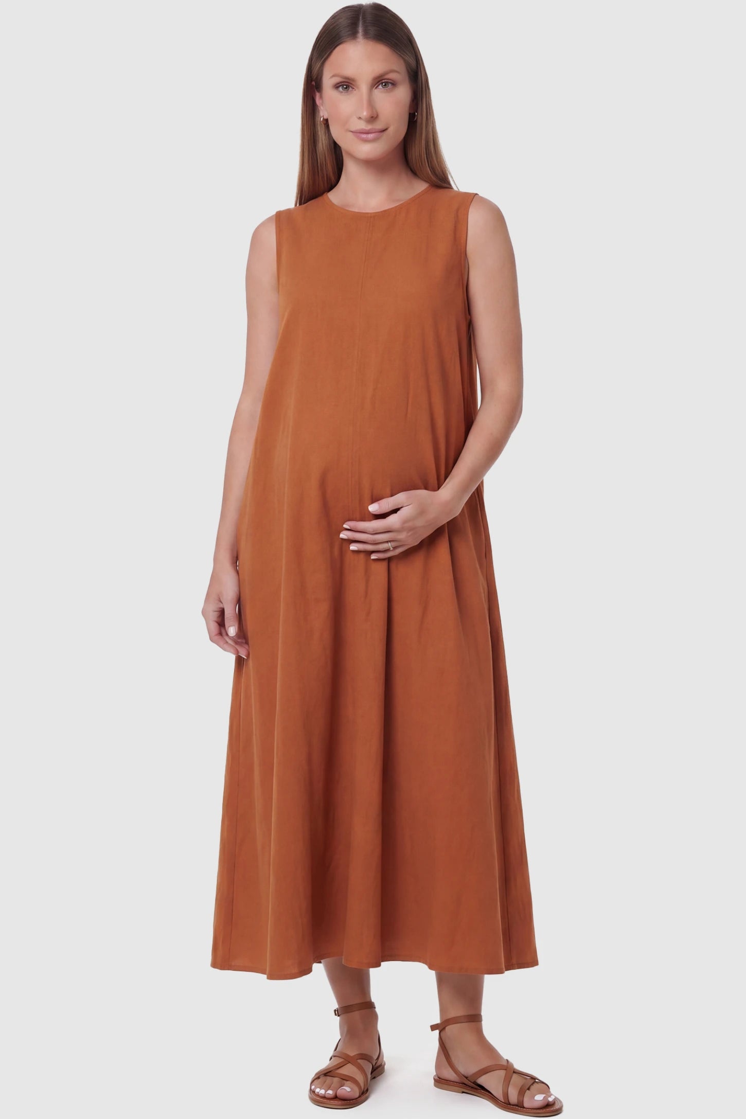 Sleeveless Pocketed Longline Hem Maternity Midi Dress Sleeveless pocketed longline hem maternity midi dress in rust brown with sleeveless design and longline hem, front view on pregnant model