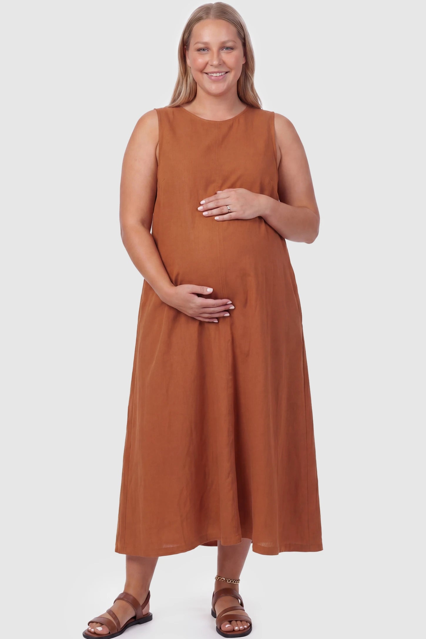Sleeveless Pocketed Longline Hem Maternity Midi Dress Sleeveless pocketed longline hem maternity midi dress in rust brown with sleeveless design and longline hem, front view on plus-size model
