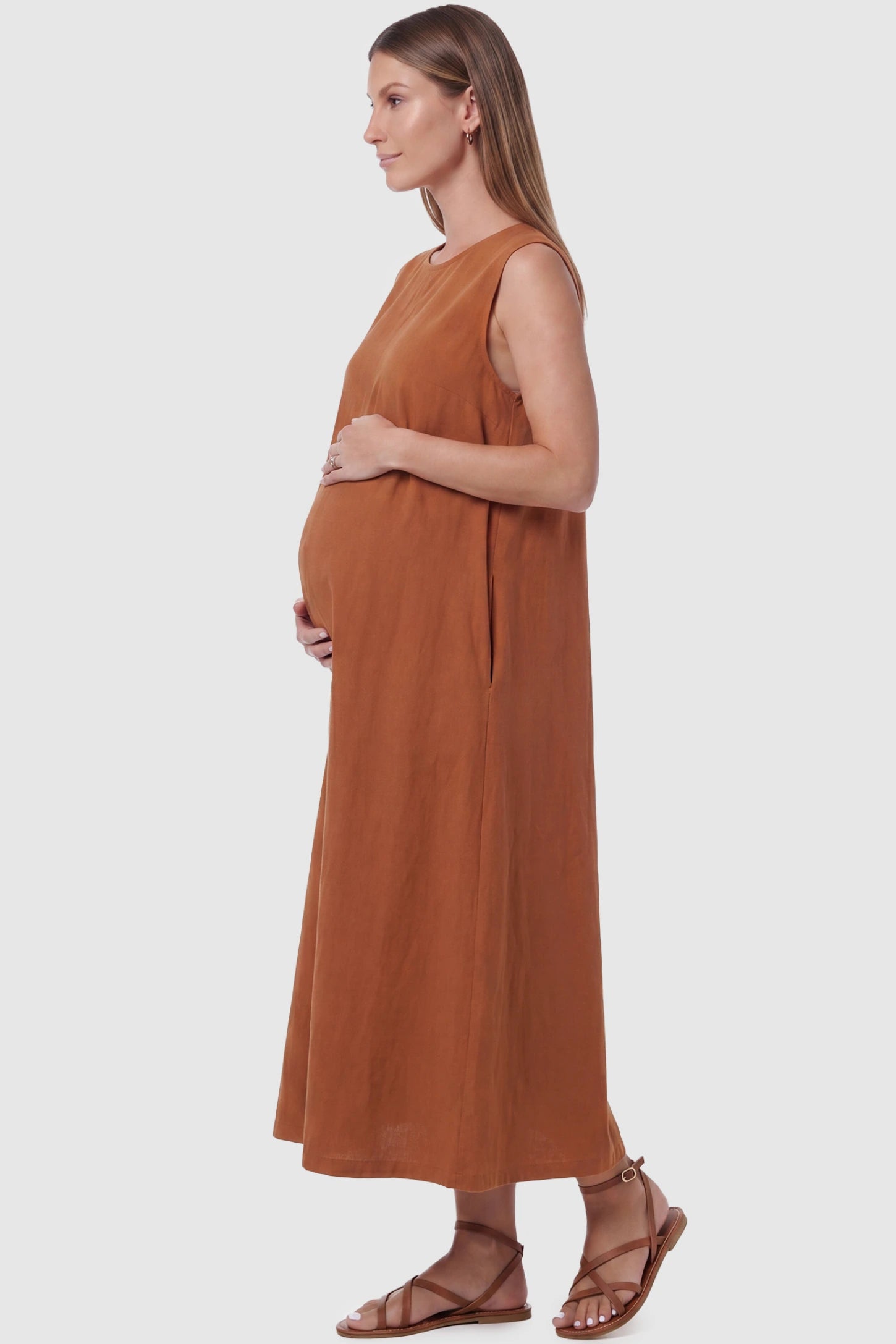 Sleeveless Pocketed Longline Hem Maternity Midi Dress Sleeveless pocketed longline hem maternity midi dress in rust brown with sleeveless design and side pocket, side view on pregnant model