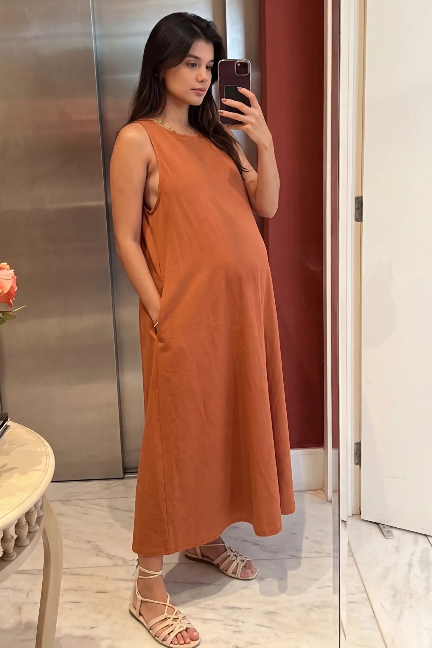 Sleeveless Pocketed Longline Hem Maternity Midi Dress Sleeveless pocketed longline hem maternity midi dress in rust brown with sleeveless design and longline hem, front view on pregnant model