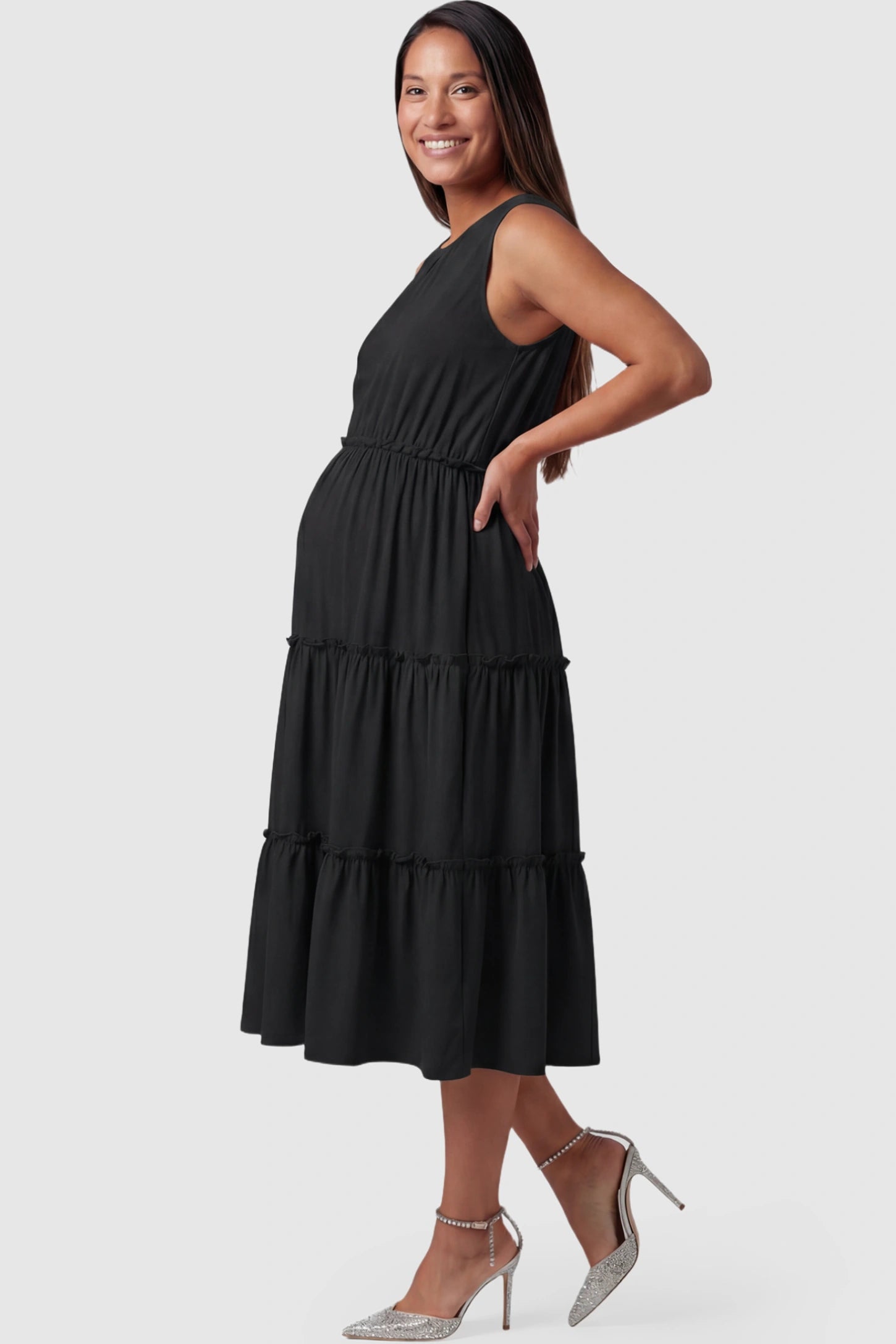 Solid Sleeveless Ruffle Tiered Maternity Midi Dress Solid Sleeveless Ruffle Tiered Maternity Midi Dress in black featuring a ruffle tiered skirt on a pregnant model showing side.