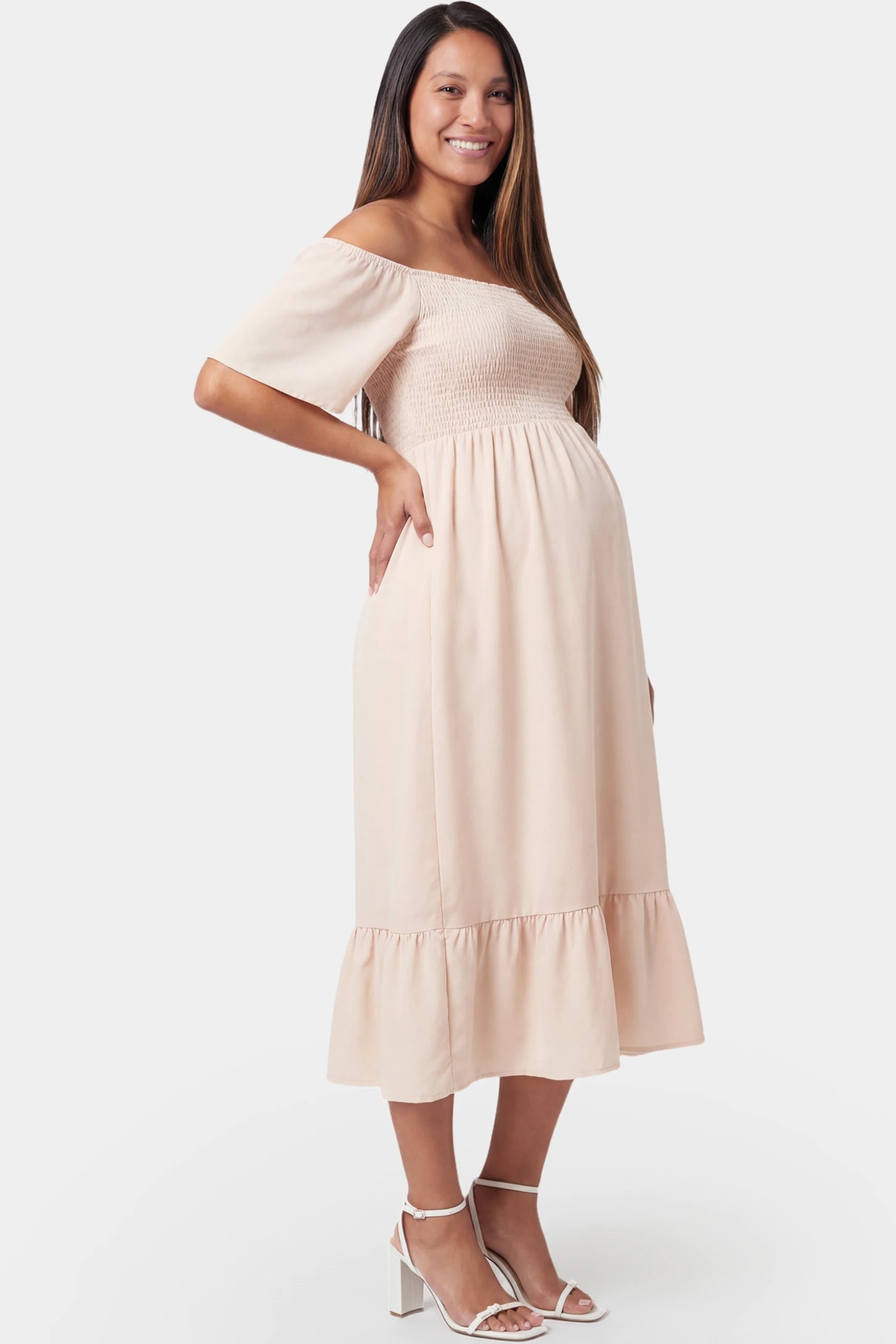 Off-Shoulder Smocked Short Sleeve A-Line Midi Maternity Dress Off-shoulder smocked short sleeve A-line midi maternity dress in apricot featuring delicate ruffle detail in side view on a pregnant model