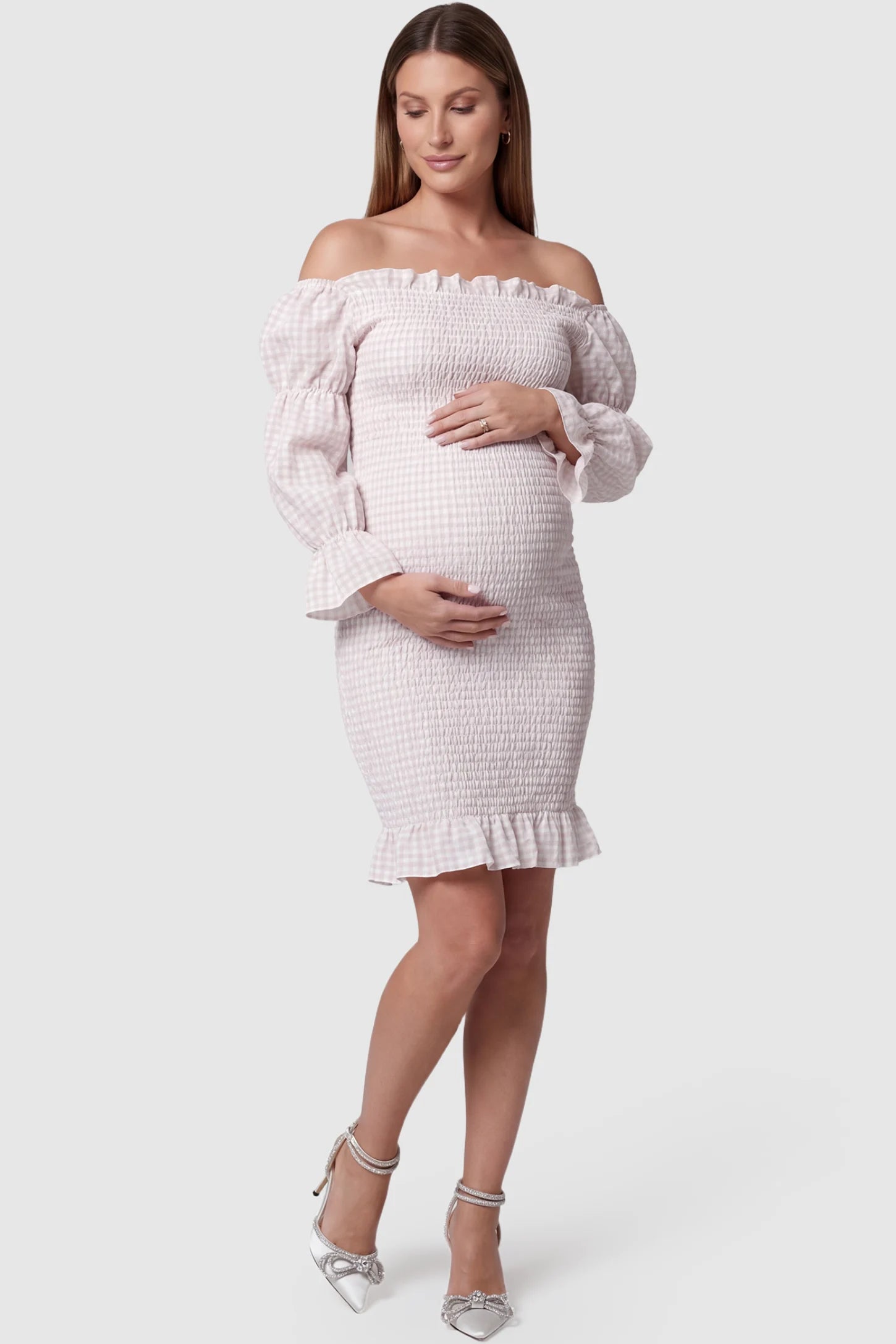 Smocked Off-Shoulder Bodycon Maternity Short Dress Smocked off-shoulder bodycon maternity short dress in white pink gingham with smocked bodice detail, front view on pregnant model