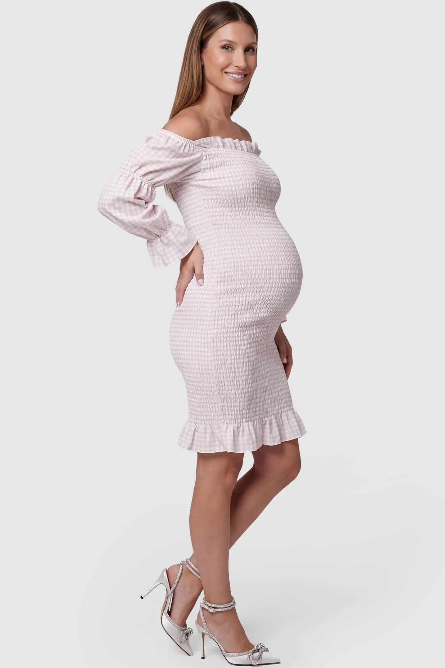 Smocked Off-Shoulder Bodycon Maternity Short Dress Smocked off-shoulder bodycon maternity short dress in white pink gingham with smocked bodice detail, side view on pregnant model
