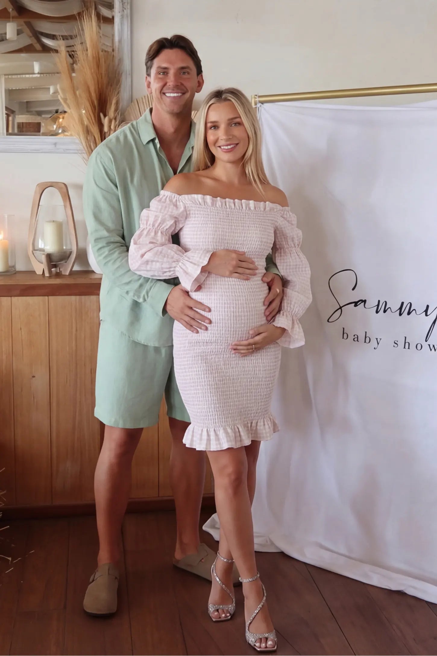 Smocked Off-Shoulder Bodycon Maternity Short Dress Smocked off-shoulder bodycon maternity short dress in white pink gingham with smocked bodice detail, front view on pregnant model
