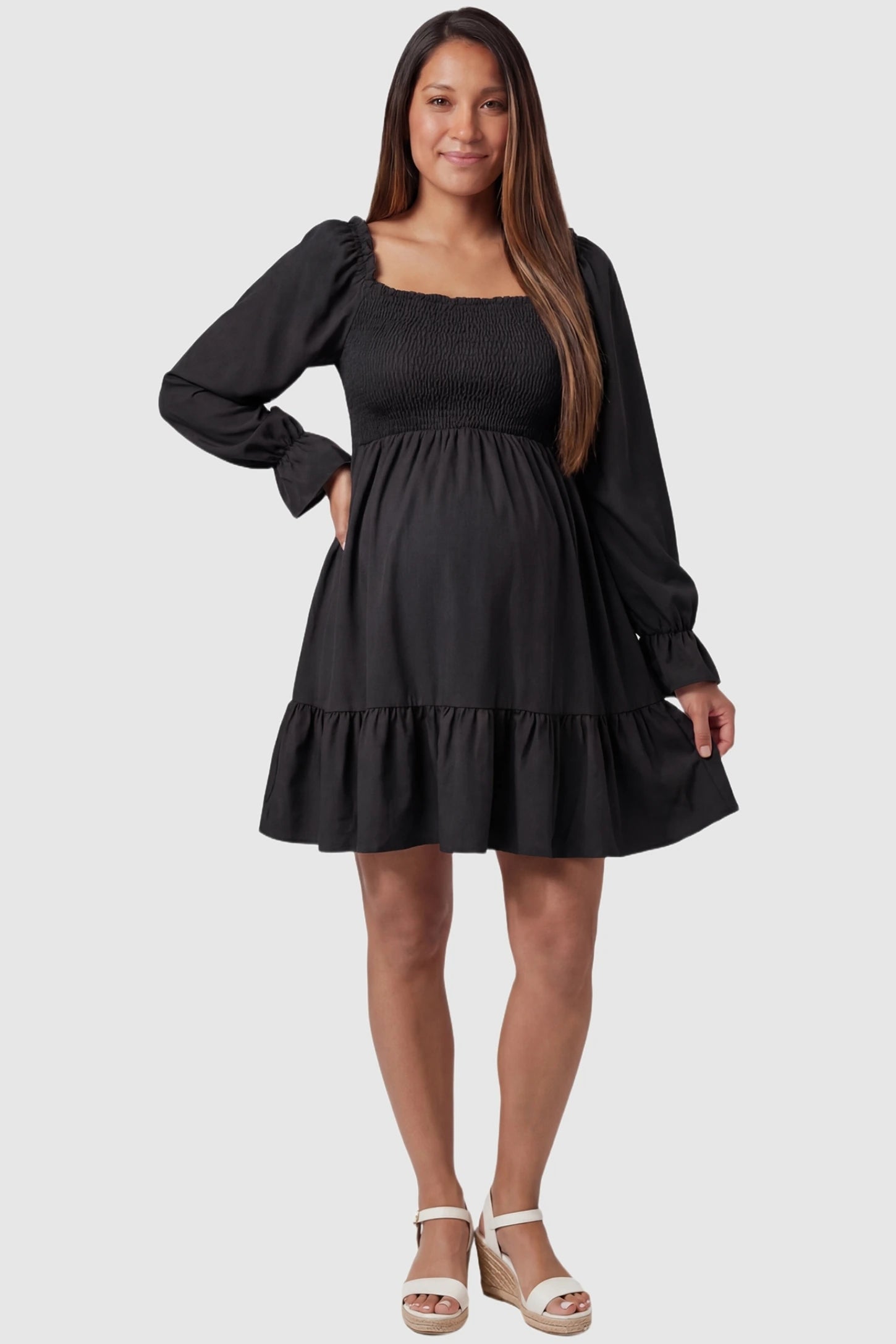 Smocked Chiffon A-Line Maternity Mini Dress in Black with a square neck and ruffle hem on a pregnant model, front view.