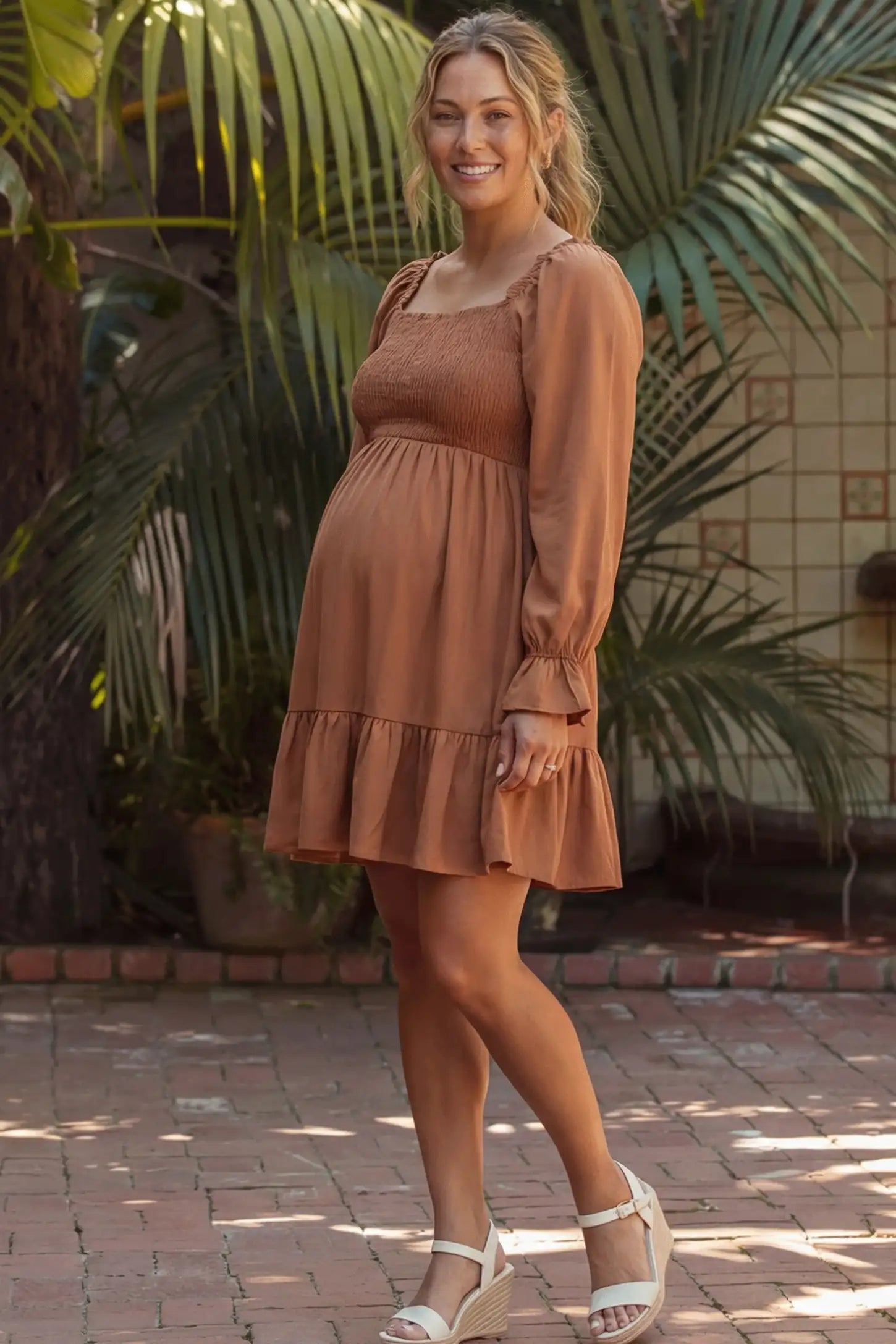 Smocked Chiffon A-Line Maternity Mini Dress Smocked Chiffon A-Line Maternity Mini Dress in Camel featuring long blouson sleeves on a side-profile pregnant model.