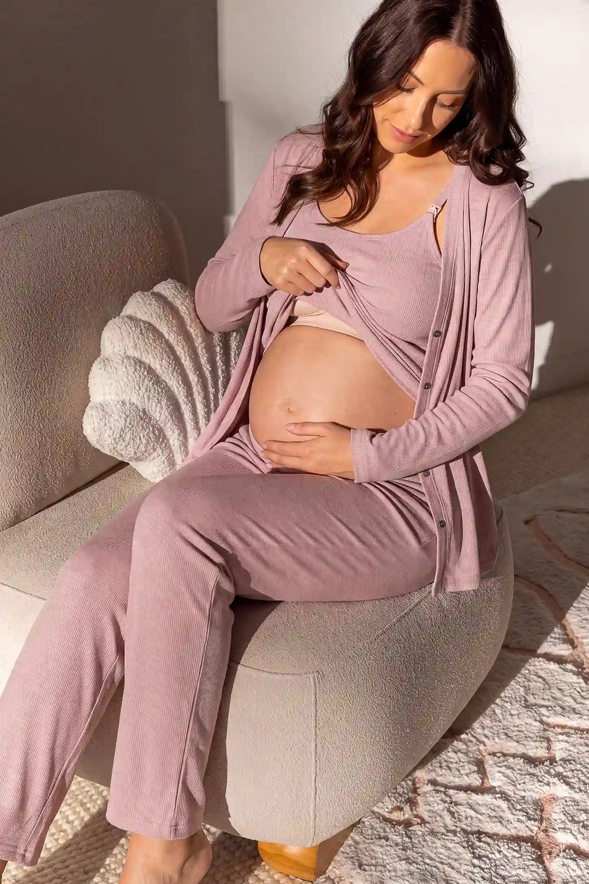 Soft Rib Knit Maternity & Nursing PJ Set with Cami, Cardigan & Pants Soft Rib Knit Maternity & Nursing Pajama Set with Cami, Cardigan & Pants in Soft Pink featuring soft strap detail, built-in fixed bust pads, and comfortable loungewear style on a pregnant model sitting down.