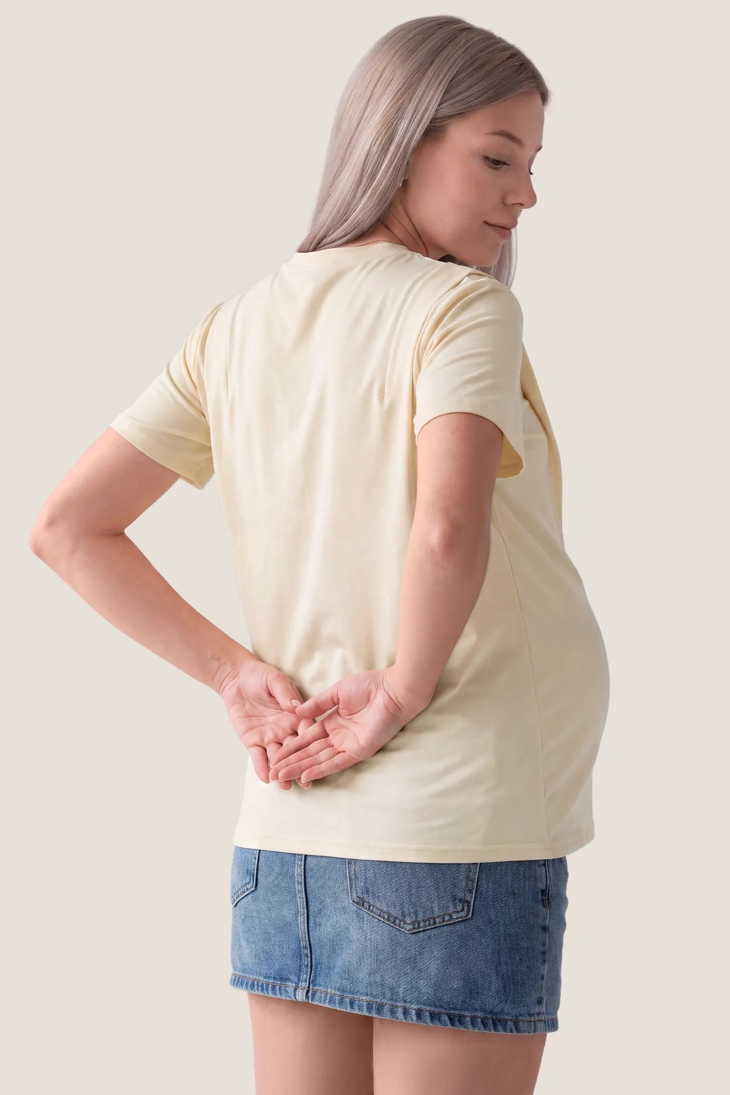 Solid Round Neck Short Sleeve Maternity Top Solid Round Neck Short Sleeve Maternity Top in Beige featuring a simple back design, soft-touch fabric, short sleeves, and a comfortable maternity silhouette on a pregnant model, back view.