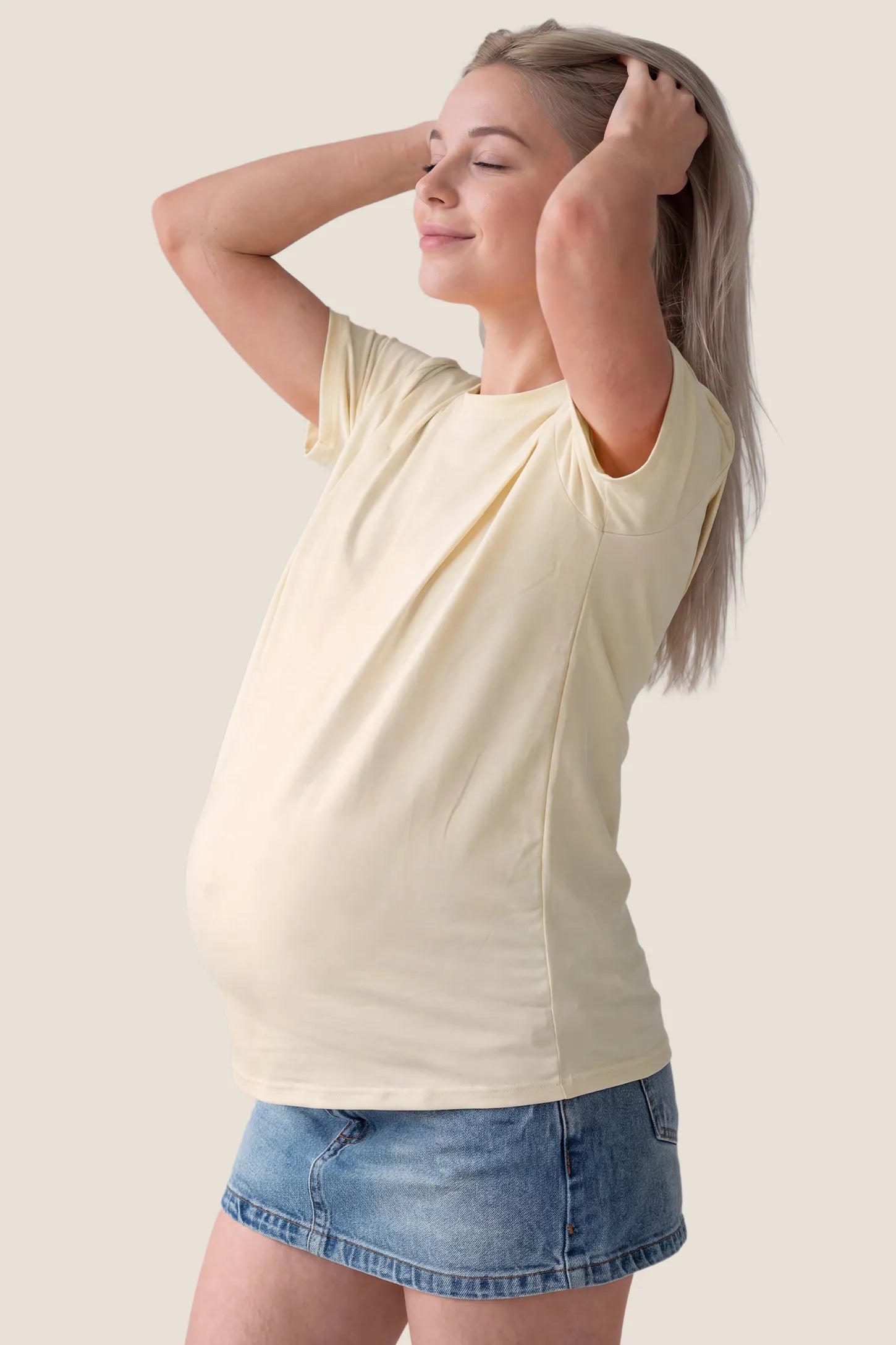 Solid Round Neck Short Sleeve Maternity Top Solid Round Neck Short Sleeve Maternity Top in Beige featuring a round neckline, soft-touch fabric, short sleeves, and a relaxed maternity-friendly silhouette on a pregnant model, side view.
