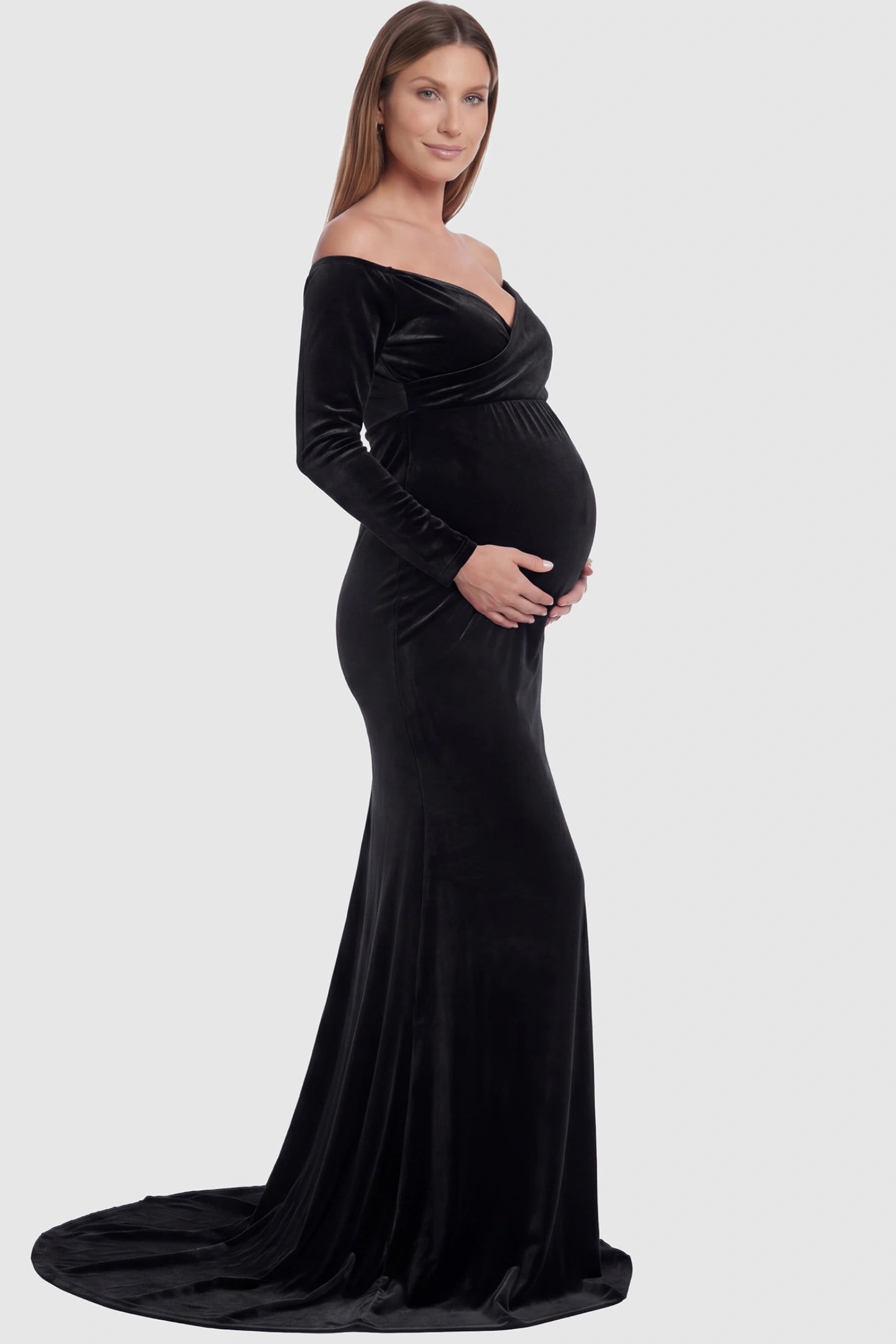 Velvet Long Fitted Sleeve Maternity Gown Velvet Long Fitted Sleeve Maternity Gown in black featuring an off-shoulder sweetheart neckline, draped bust, empire waist, and mermaid skirt on pregnant model side view.