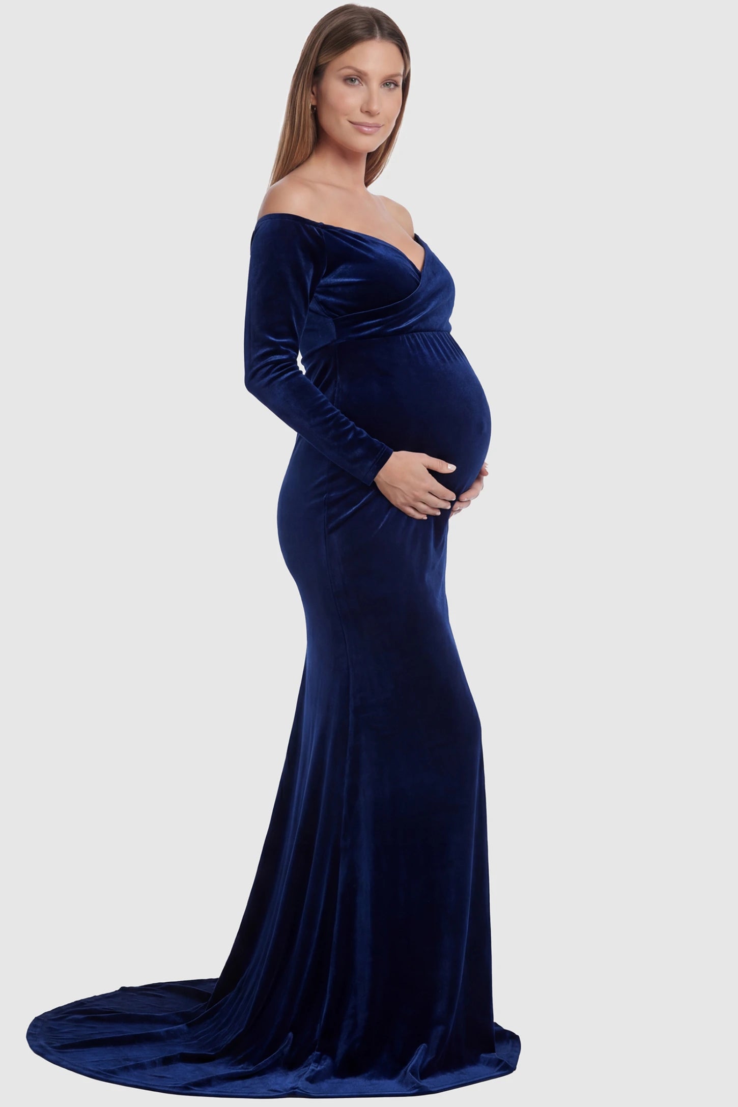 Velvet Long Fitted Sleeve Maternity Gown Velvet Long Fitted Sleeve Maternity Gown in navy blue featuring an off-shoulder sweetheart neckline, draped bust, empire waist, and mermaid skirt on pregnant model side view.