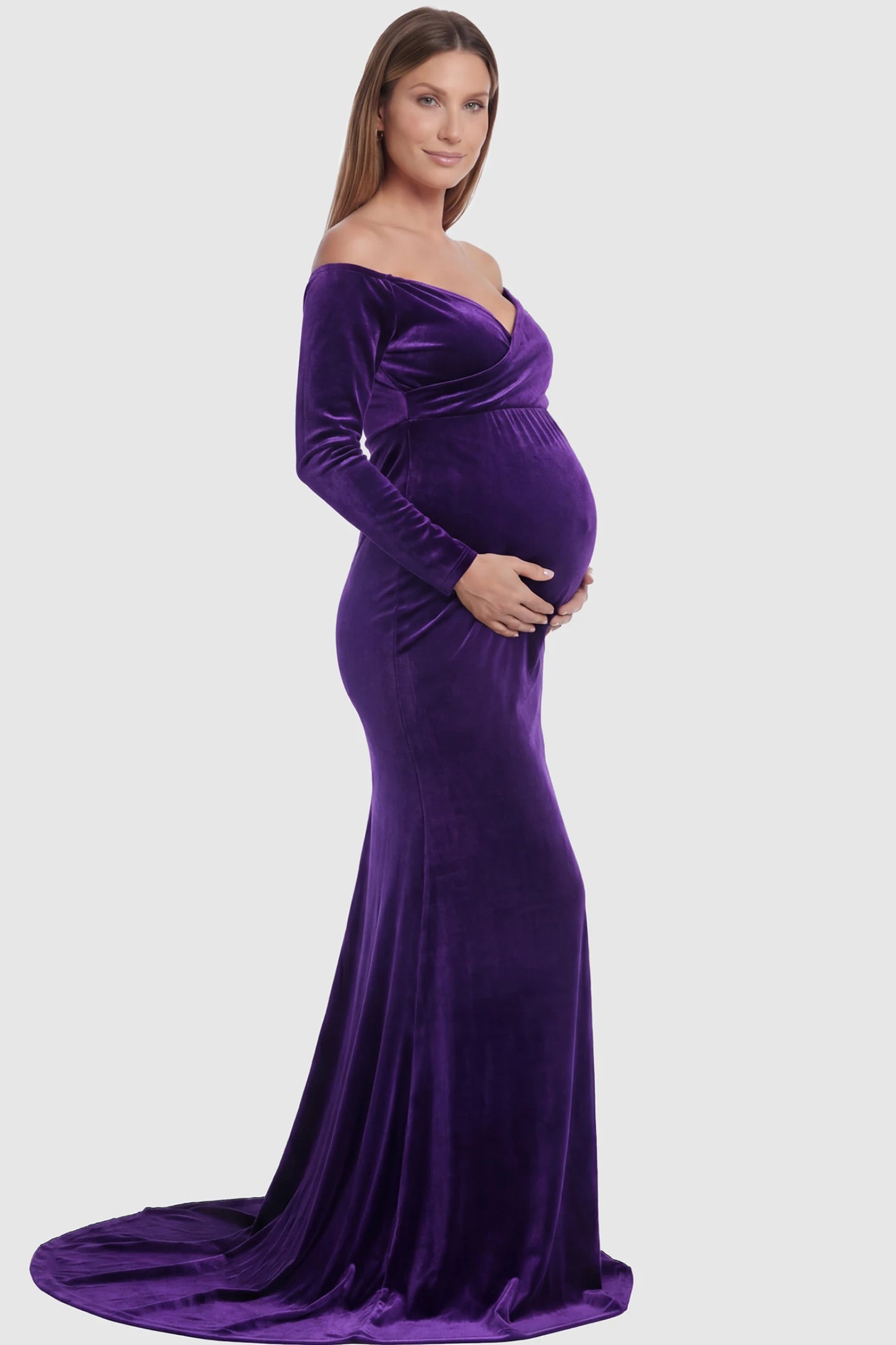 Velvet Long Fitted Sleeve Maternity Gown Velvet Long Fitted Sleeve Maternity Gown in purple featuring an off-shoulder sweetheart neckline, draped bust, empire waist, and mermaid skirt on pregnant model side view.