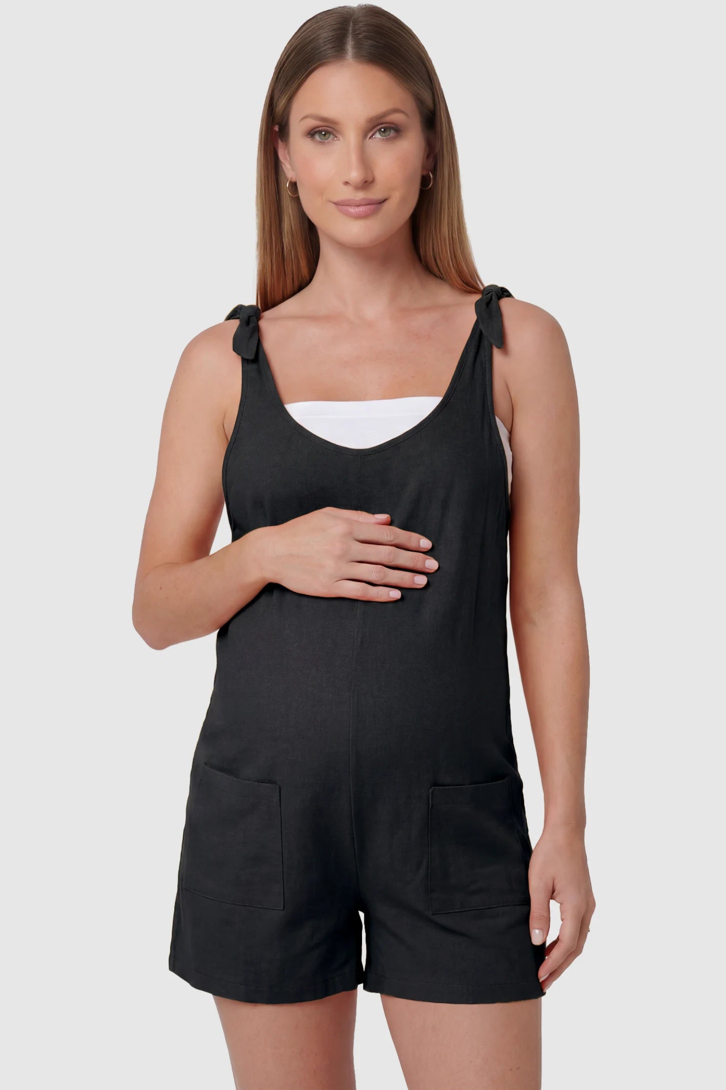 Tie-Strap Sleeveless Pocketed Maternity Romper Tie-strap sleeveless pocketed maternity romper in black with adjustable tie straps and scoop neckline, front view on pregnant model