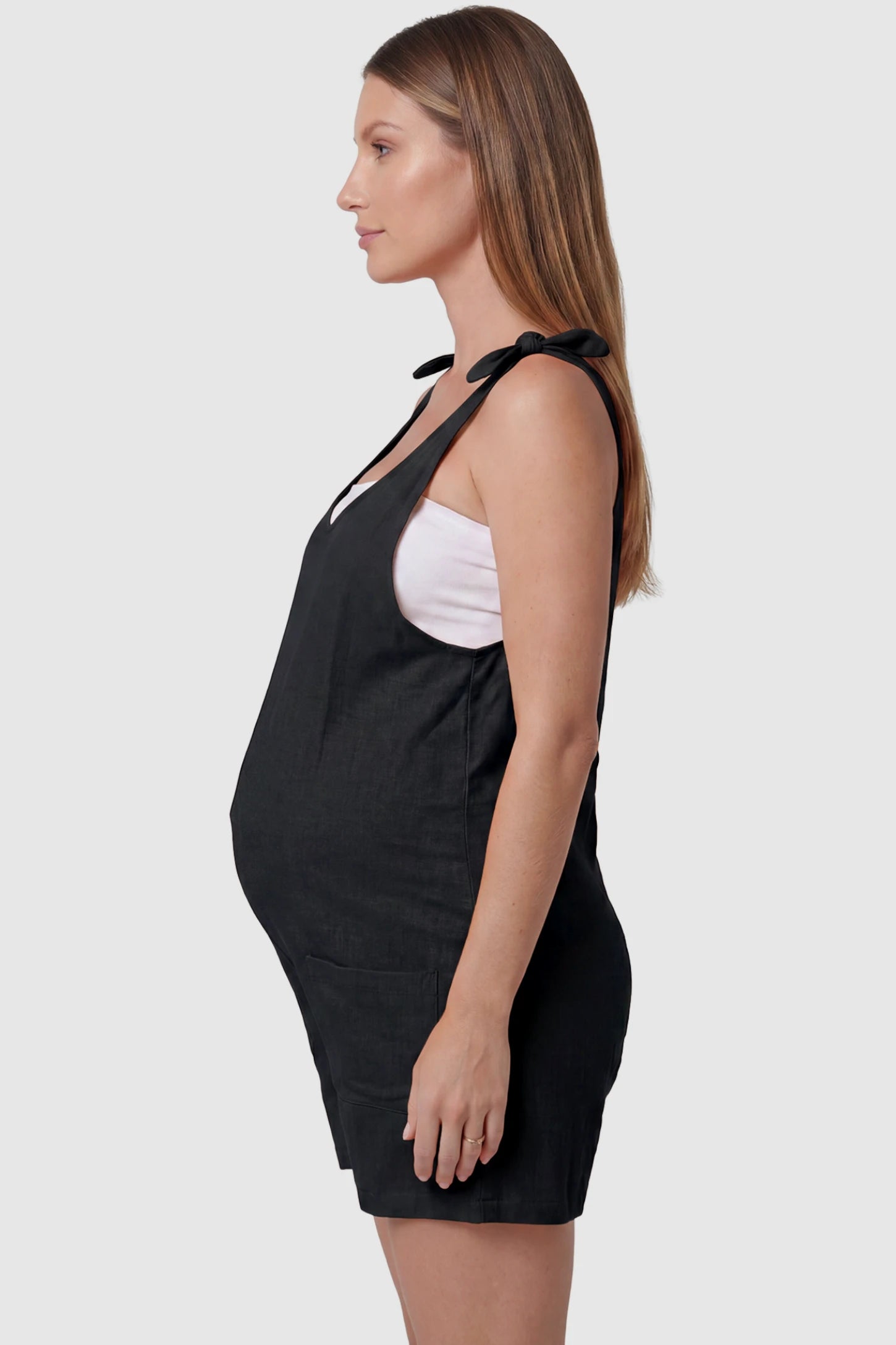 Tie-Strap Sleeveless Pocketed Maternity Romper Tie-strap sleeveless pocketed maternity romper in black with adjustable tie straps and sleeveless cut, side view on pregnant model