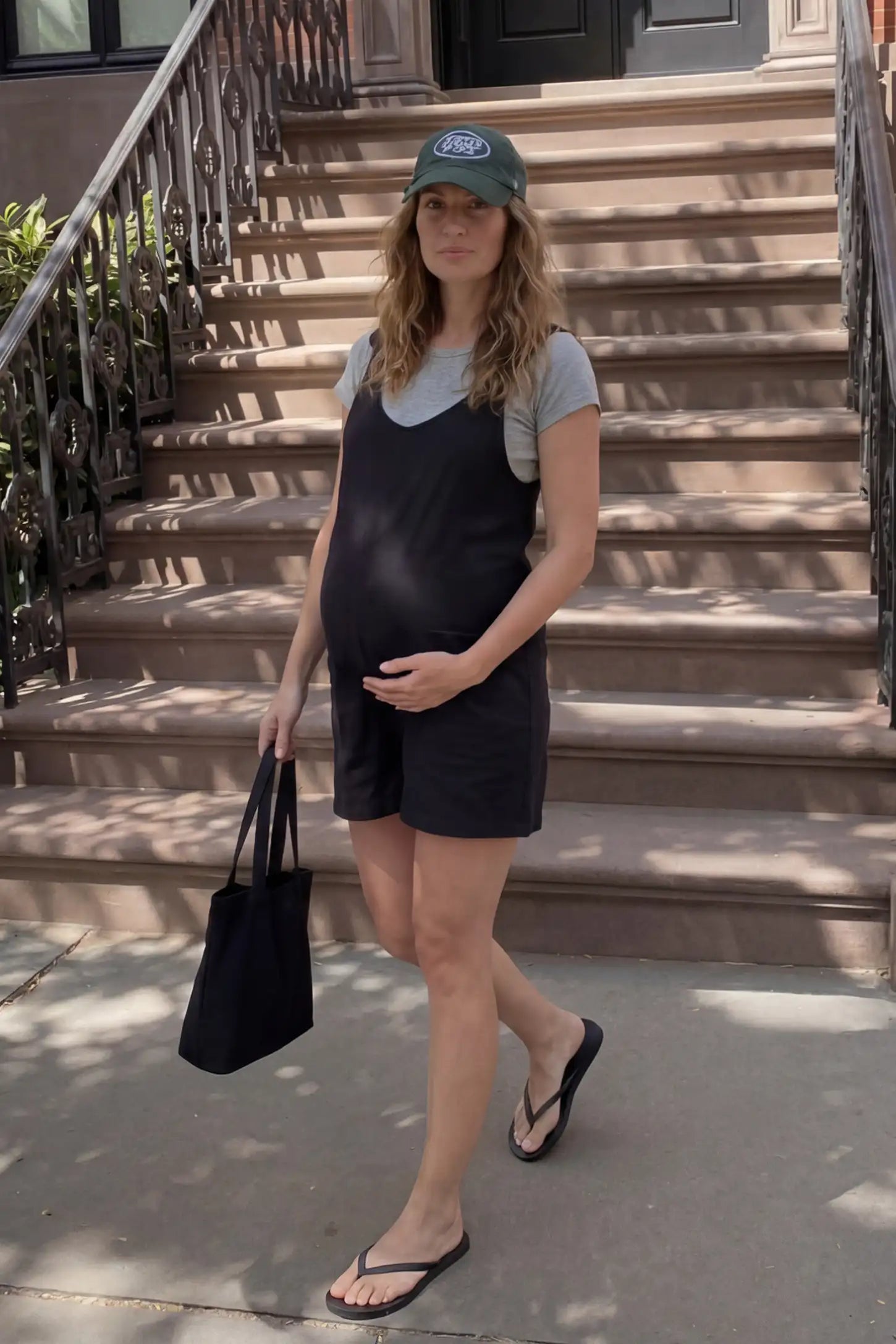 Tie-Strap Sleeveless Pocketed Maternity Romper Tie-strap sleeveless pocketed maternity romper in black with adjustable tie straps and scoop neckline, front view on pregnant model