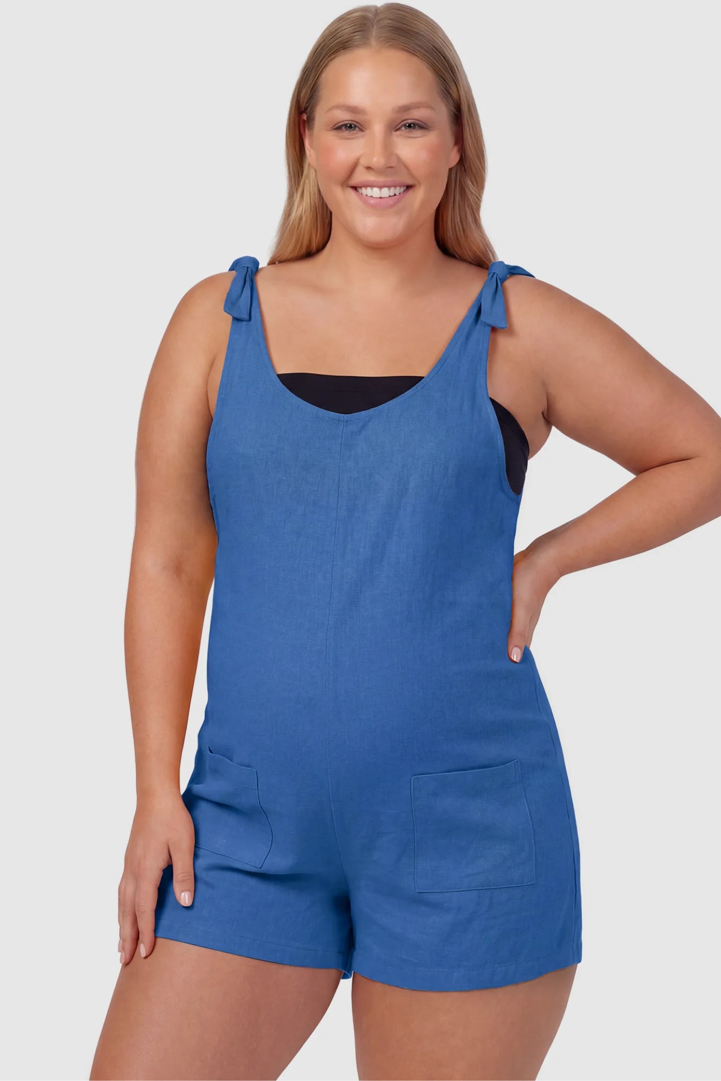 Tie-Strap Sleeveless Pocketed Maternity Romper Tie-strap sleeveless pocketed maternity romper in blue with adjustable tie straps and scoop neckline, front view on plus-size model