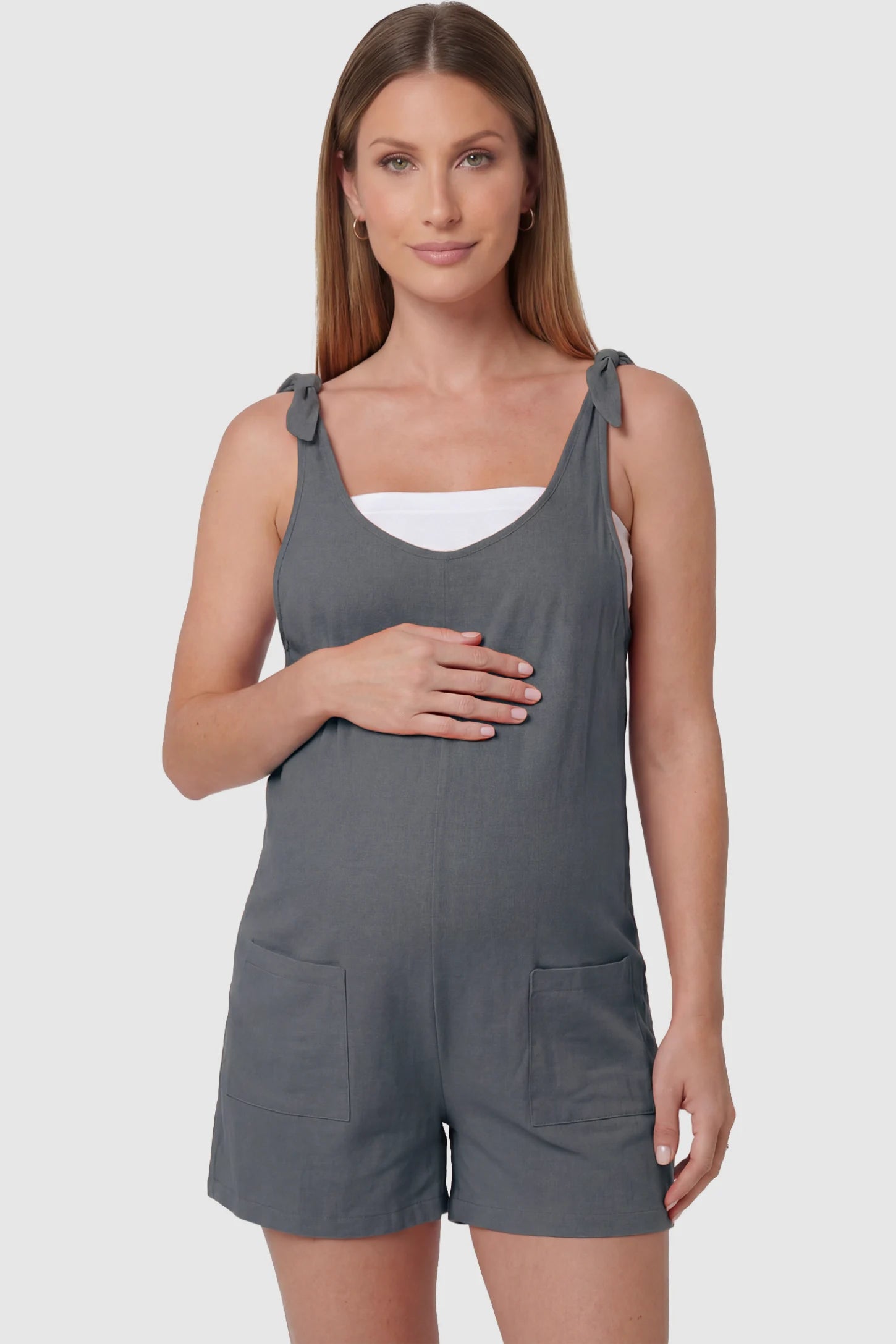 Tie-Strap Sleeveless Pocketed Maternity Romper Tie-strap sleeveless pocketed maternity romper in gray with adjustable tie straps and scoop neckline, front view on pregnant model