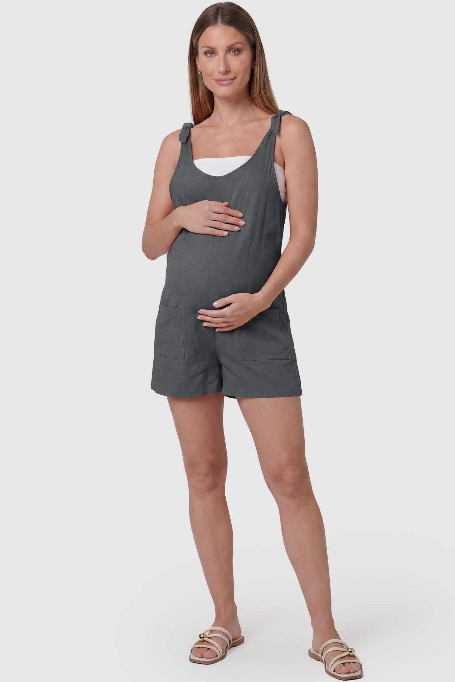 Tie-Strap Sleeveless Pocketed Maternity Romper Tie-strap sleeveless pocketed maternity romper in gray with adjustable tie straps and scoop neckline, front view on pregnant model