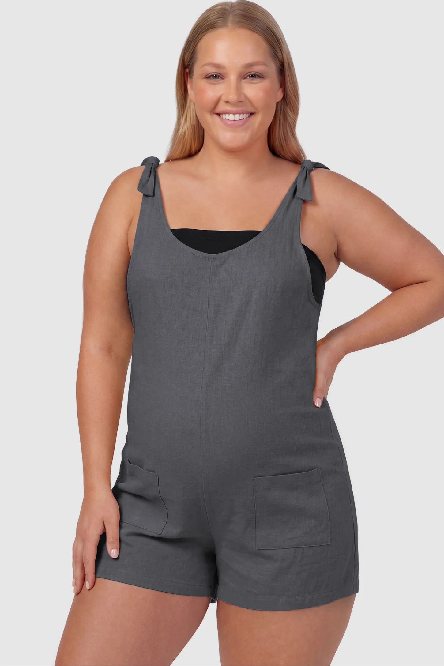Tie-Strap Sleeveless Pocketed Maternity Romper Tie-strap sleeveless pocketed maternity romper in gray with adjustable tie straps and scoop neckline, front view on plus-size model