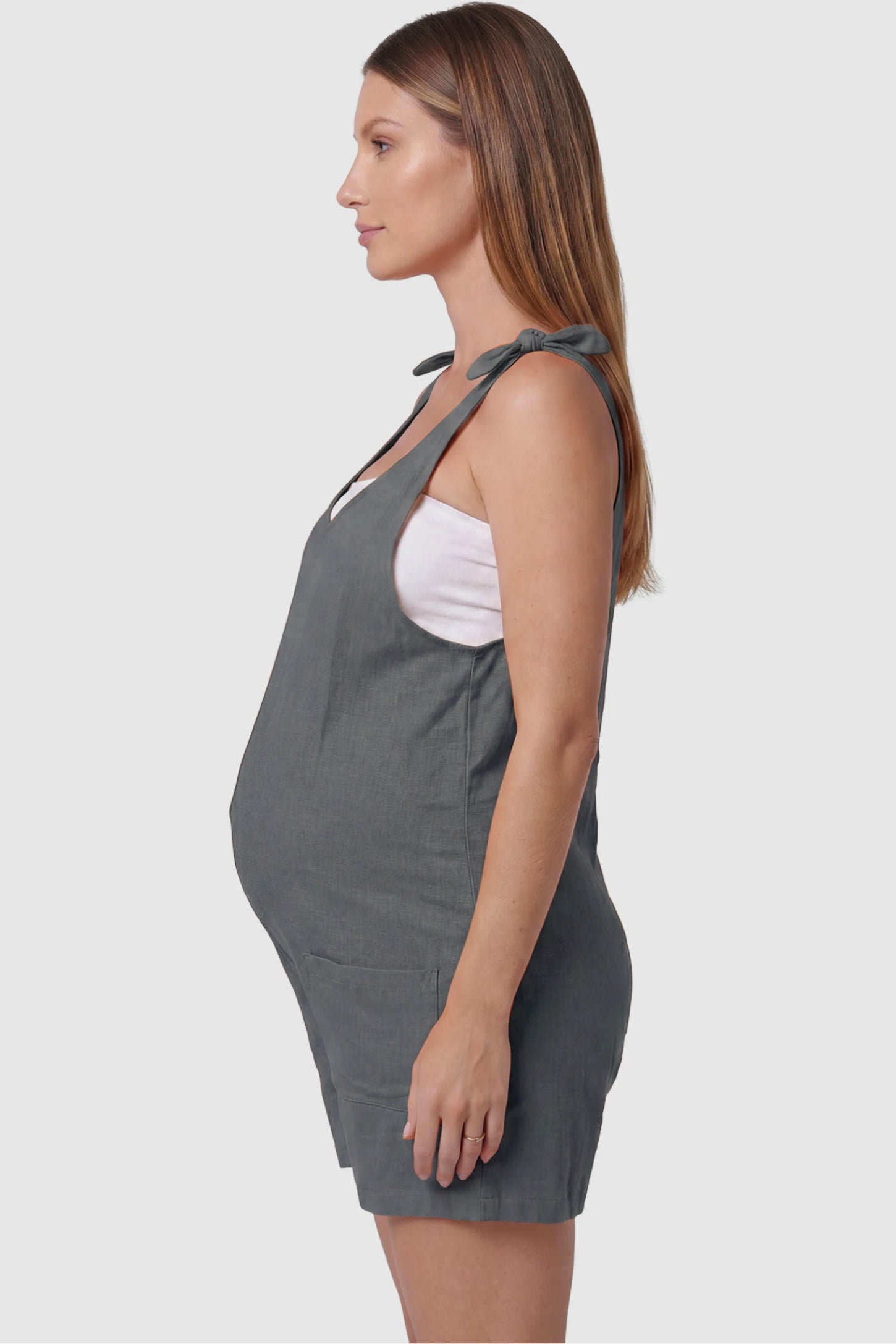Tie-Strap Sleeveless Pocketed Maternity Romper Tie-strap sleeveless pocketed maternity romper in gray with adjustable tie straps and sleeveless cut, side view on pregnant model