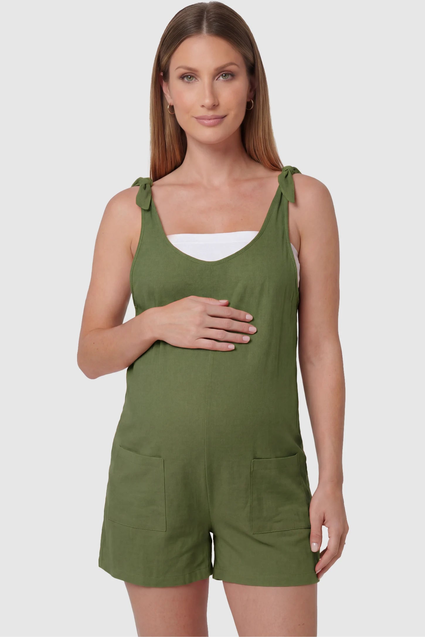 Tie-Strap Sleeveless Pocketed Maternity Romper Tie-strap sleeveless pocketed maternity romper in green with adjustable tie straps and scoop neckline, front view on pregnant model