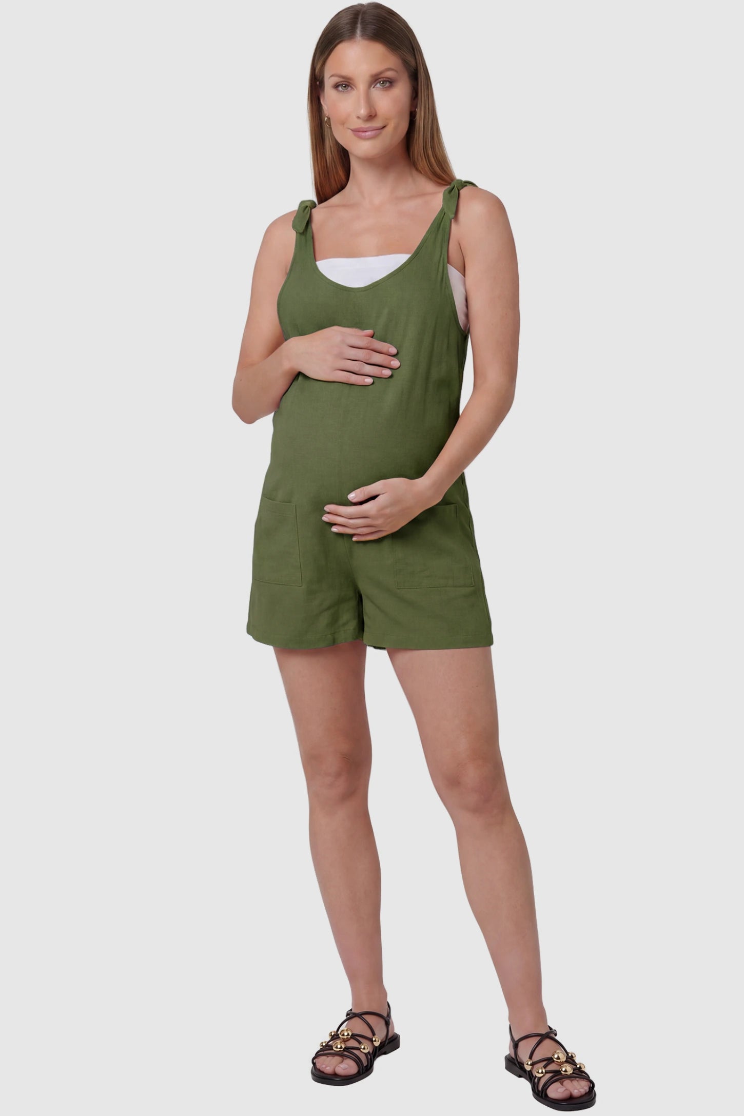 Tie-Strap Sleeveless Pocketed Maternity Romper Tie-strap sleeveless pocketed maternity romper in green with adjustable tie straps and scoop neckline, front view on pregnant model