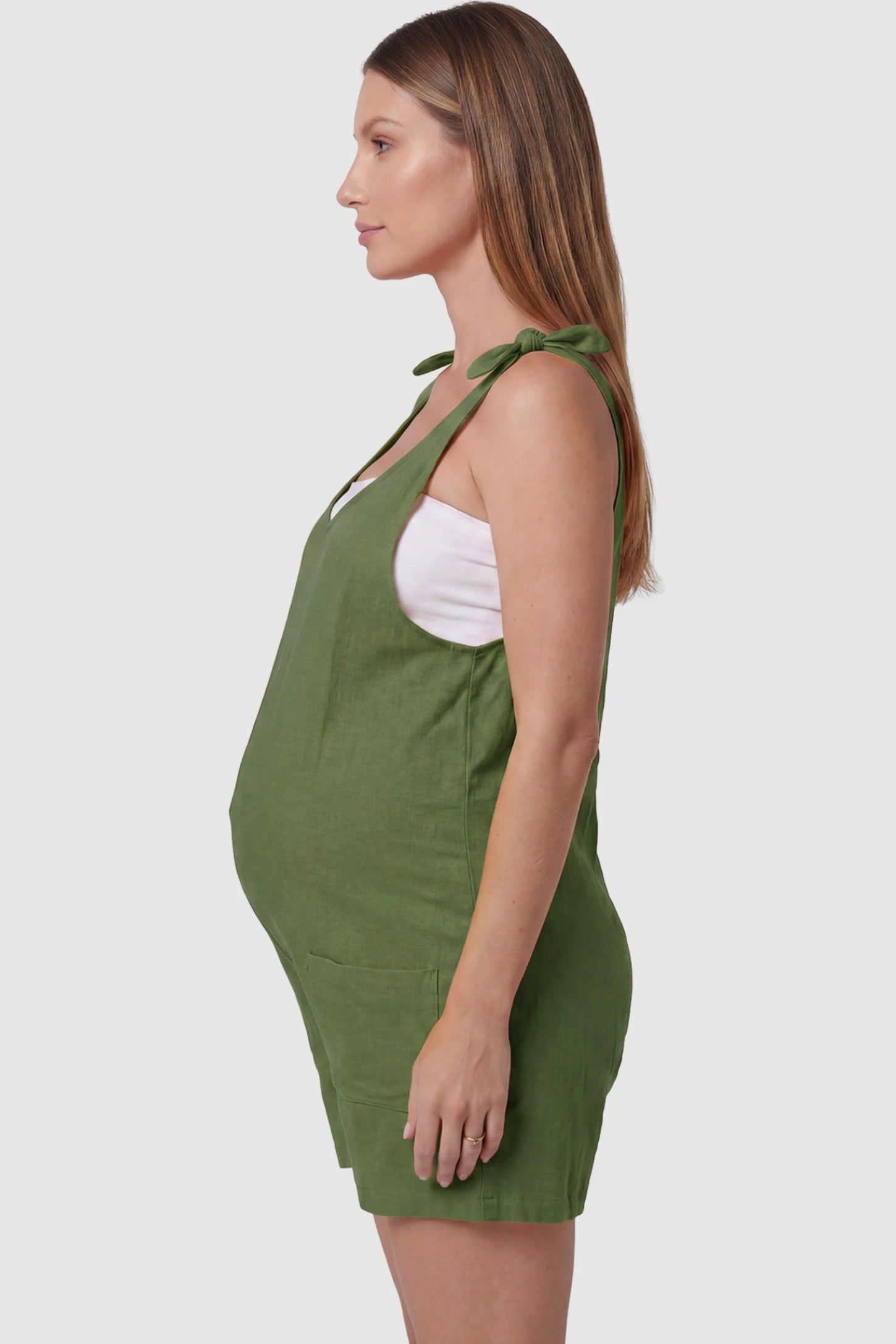Tie-Strap Sleeveless Pocketed Maternity Romper Tie-strap sleeveless pocketed maternity romper in green with adjustable tie straps and sleeveless cut, side view on pregnant model
