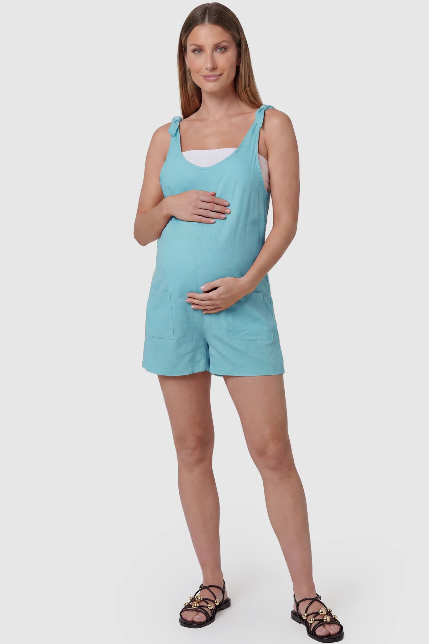Tie-Strap Sleeveless Pocketed Maternity Romper Tie-strap sleeveless pocketed maternity romper in sky blue with adjustable tie straps and scoop neckline, front view on pregnant model