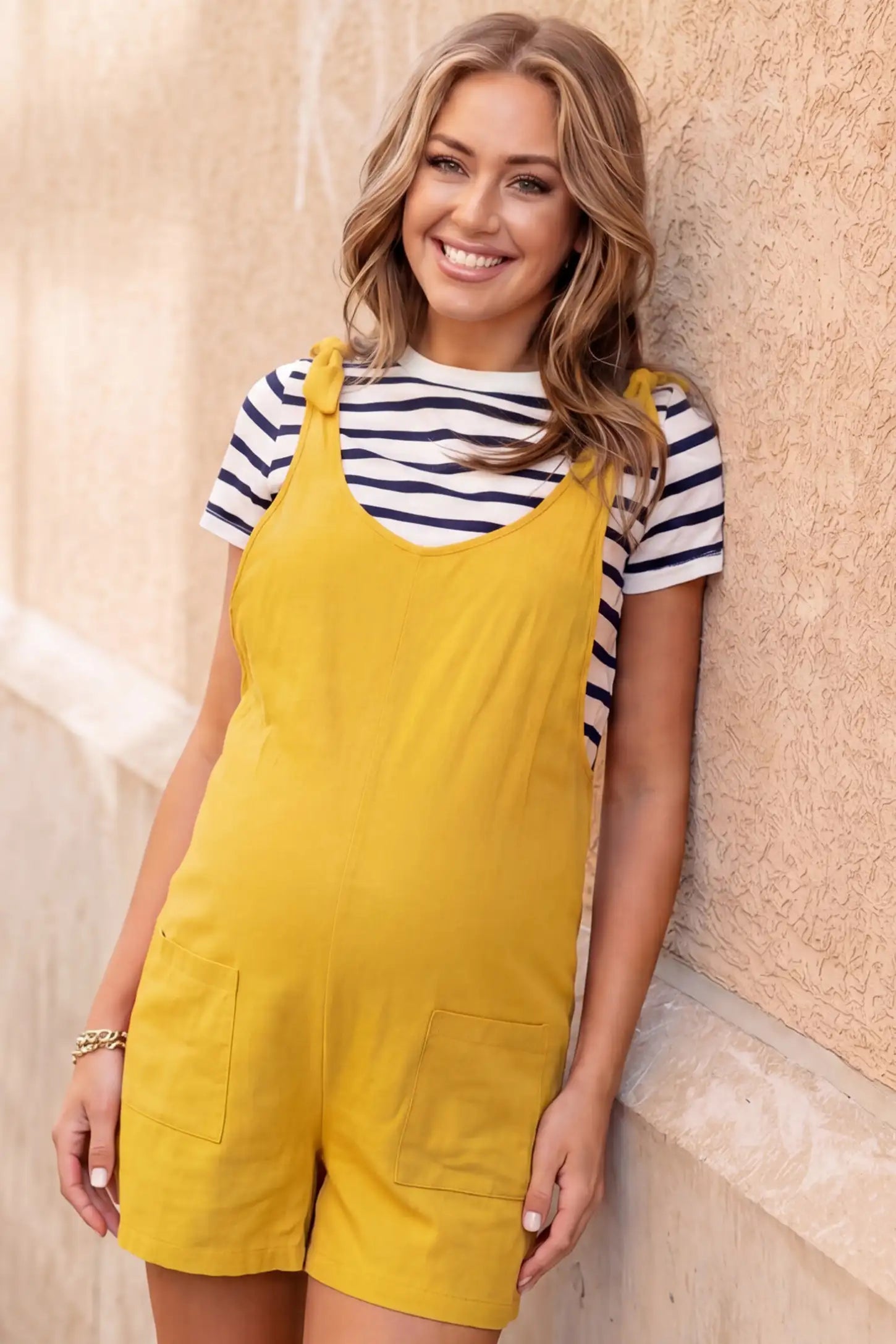 Tie-Strap Sleeveless Pocketed Maternity Romper Tie-strap sleeveless pocketed maternity romper in yellow with adjustable tie straps and scoop neckline, front view on pregnant model