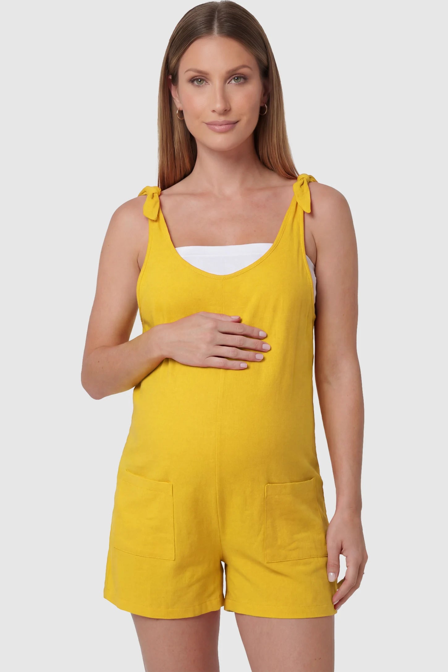 Tie-Strap Sleeveless Pocketed Maternity Romper Tie-strap sleeveless pocketed maternity romper in yellow with adjustable tie straps and scoop neckline, front view on pregnant model