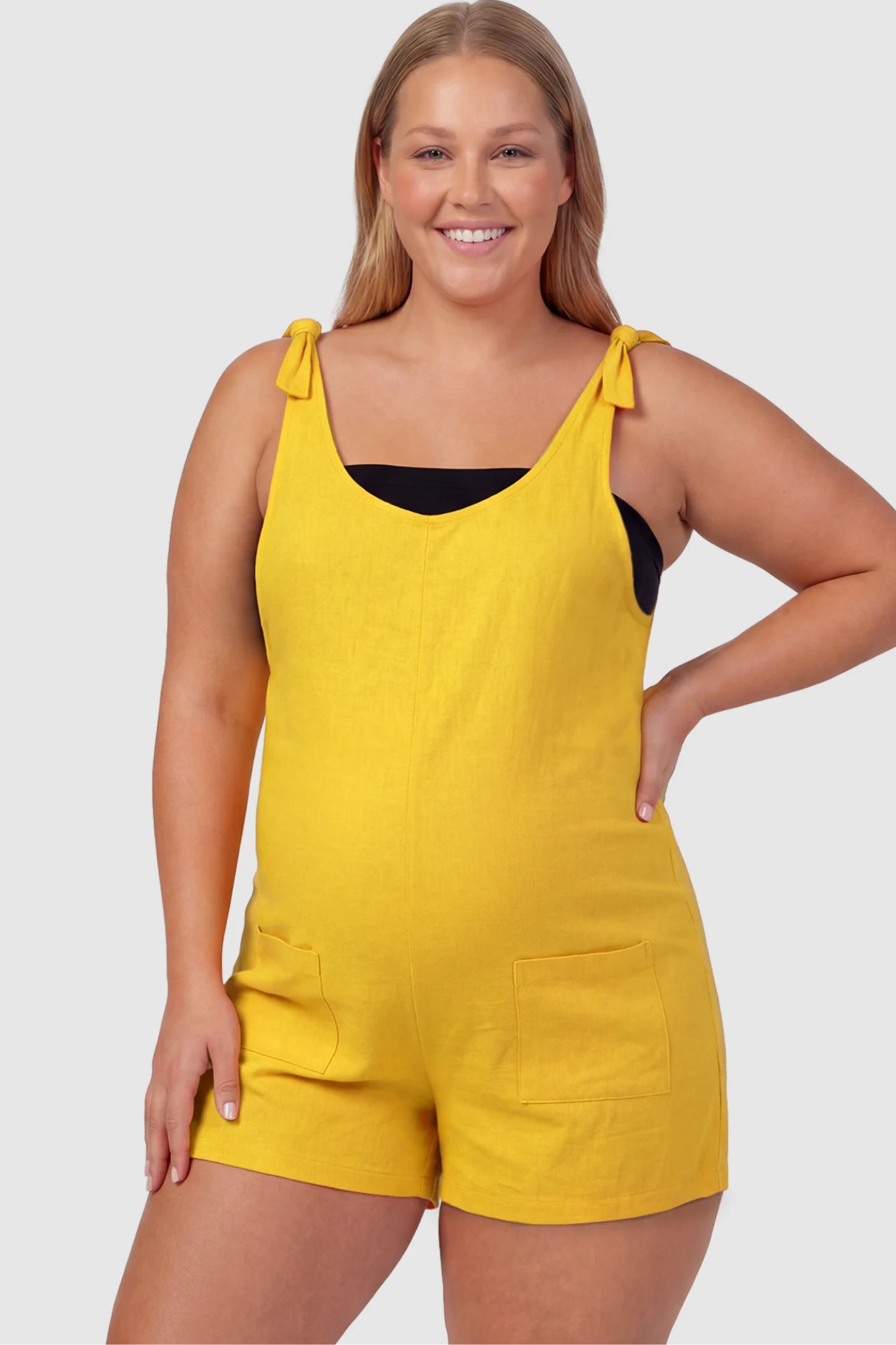 Tie-Strap Sleeveless Pocketed Maternity Romper Tie-strap sleeveless pocketed maternity romper in yellow with adjustable tie straps and scoop neckline, front view on plus-size model