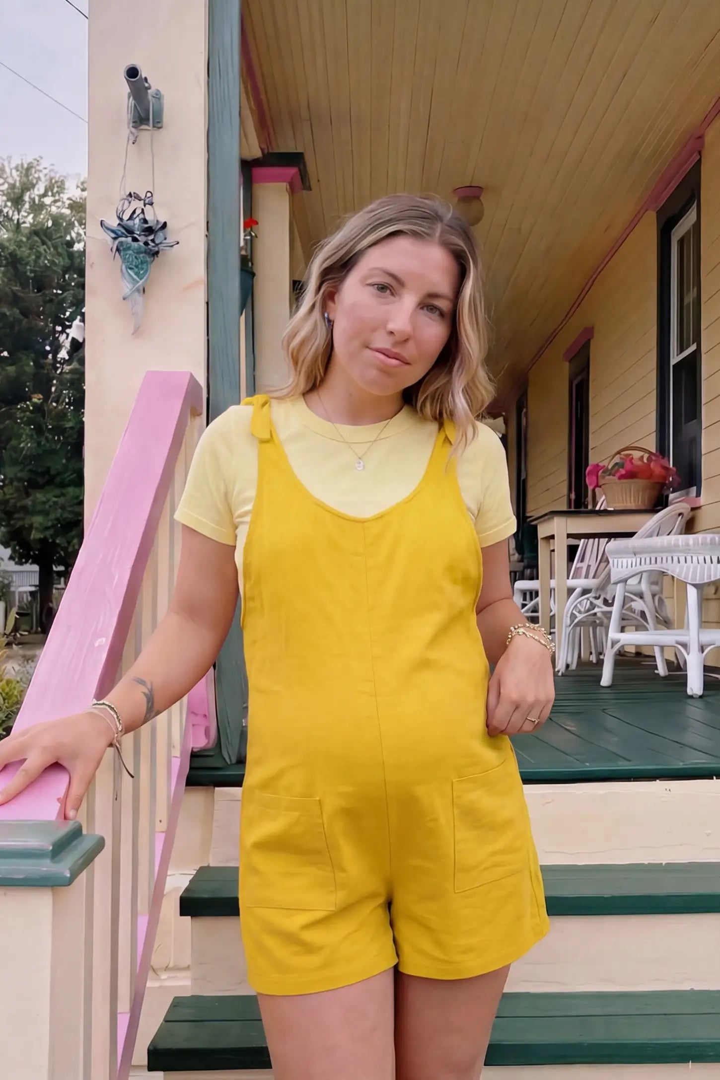 Tie-Strap Sleeveless Pocketed Maternity Romper Tie-strap sleeveless pocketed maternity romper in yellow with adjustable tie straps and scoop neckline, front view on pregnant model