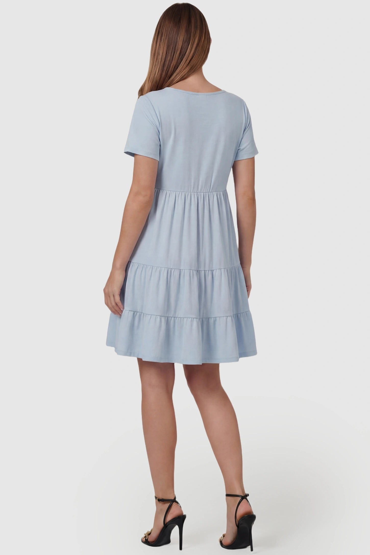Tiered Button-Front A-Line Maternity Summer Dress Tiered Button-Front A-Line Maternity Summer Dress in Light Blue featuring a flowy tiered skirt on a pregnant model, back view.