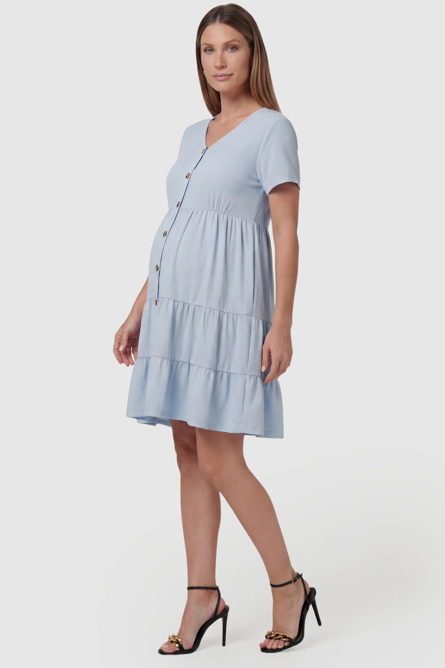 Tiered Button-Front A-Line Maternity Summer Dress Tiered Button-Front A-Line Maternity Summer Dress in Light Blue featuring short sleeves on a pregnant model, side view.
