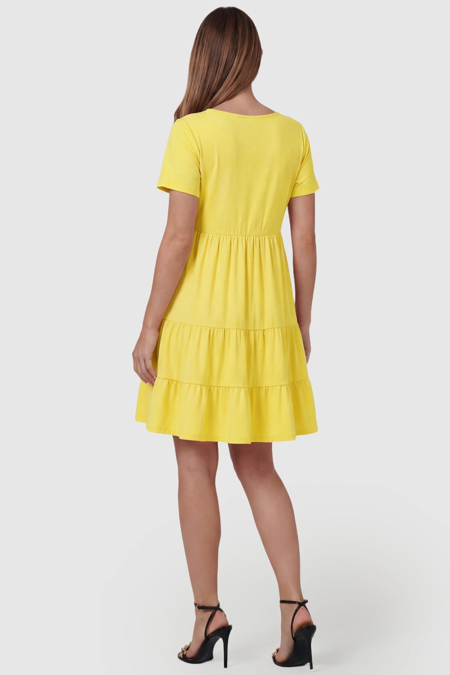 Tiered Button-Front A-Line Maternity Summer Dress Tiered Button-Front A-Line Maternity Summer Dress in Yellow featuring a breezy ruffled hem on a pregnant model, back view.