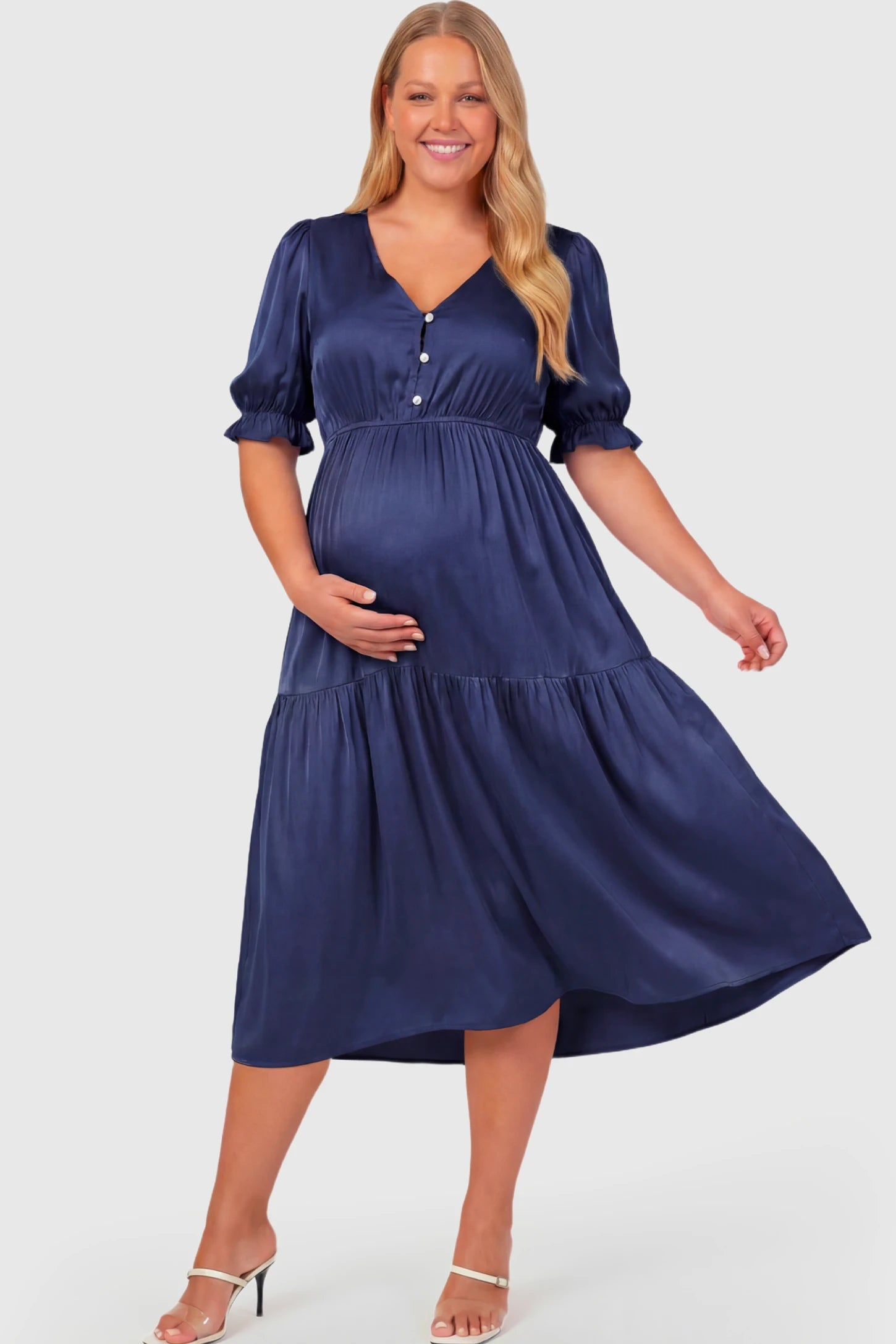 Tiered Hem A-Line Maternity Midi Dress Tiered Hem A-Line Maternity Midi Dress in navy blue featuring empire waist, elbow-length puff sleeves, V-neckline, and flowy skirt on plus size pregnant model.