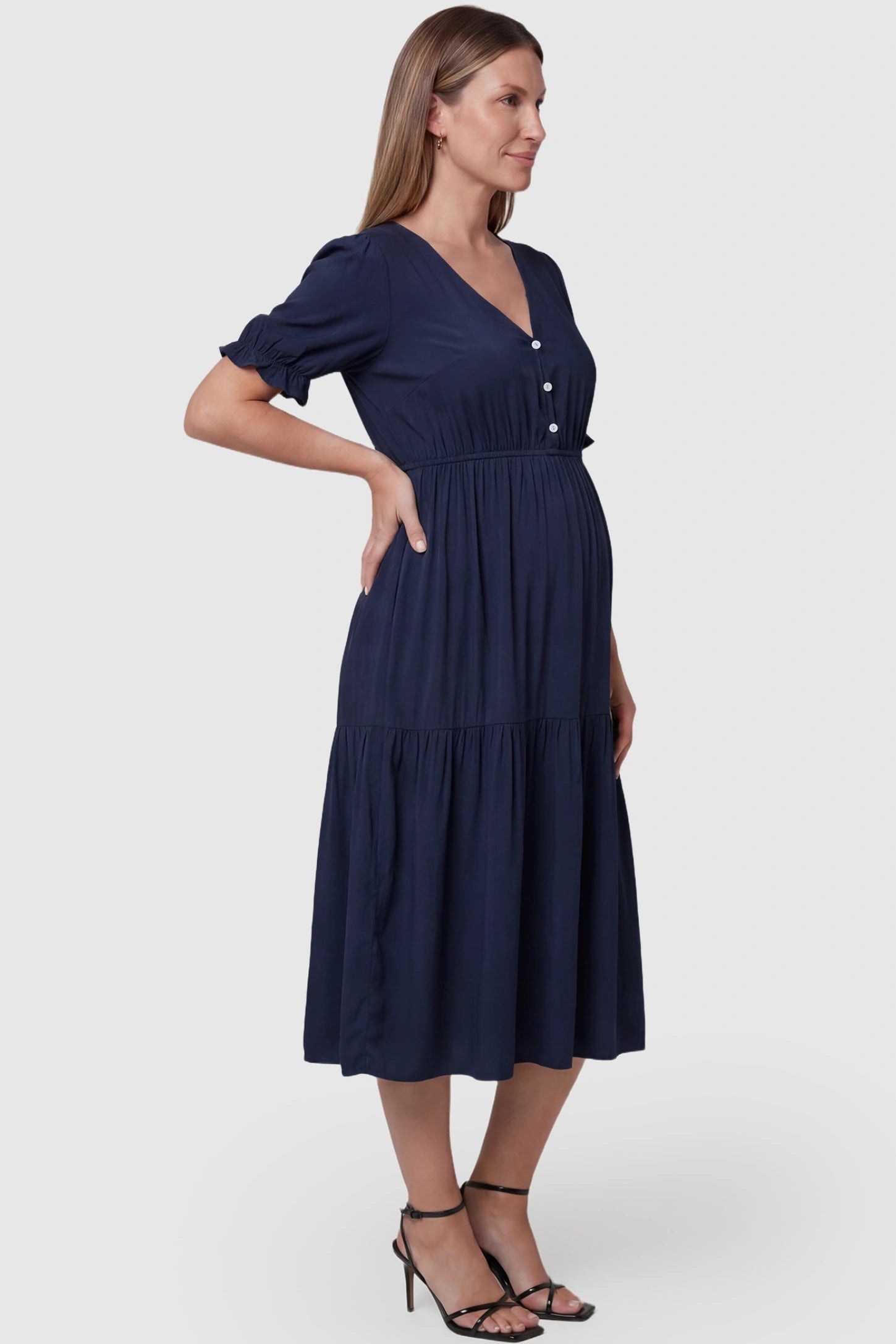 Tiered Hem A-Line Maternity Midi Dress  Tiered Hem A-Line Maternity Midi Dress in navy blue featuring empire waist, elbow-length puff sleeves, V-neckline, and flowy skirt on pregnant model. side view