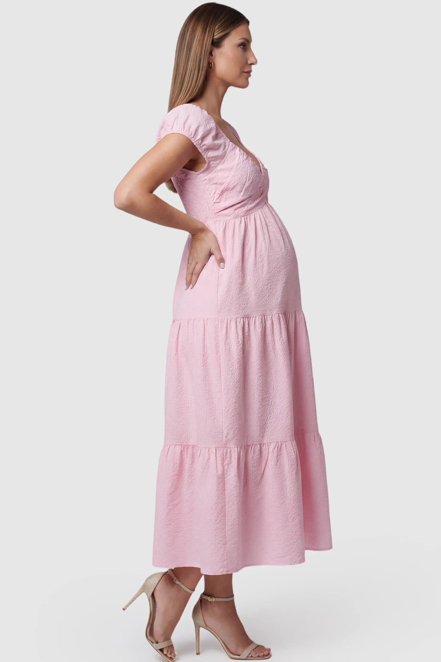 Short Puff Sleeve Tiered Maternity Maxi Dress Short Puff Sleeve Tiered Maternity Maxi Dress in pink featuring short sleeves and tiered maternity dress on a pregnant model showing side.