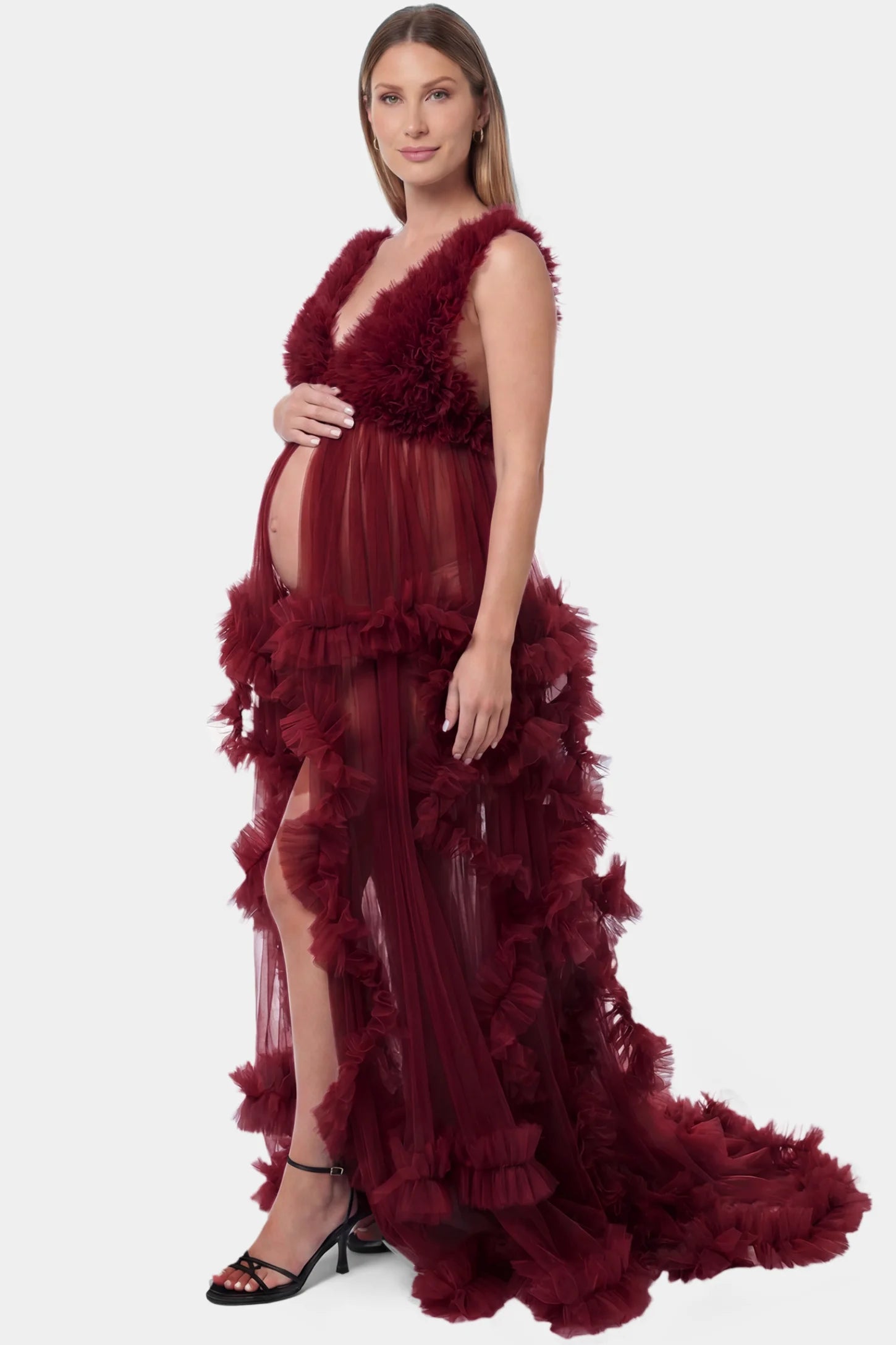 Multi-Layered Tulle Deep V-Neck Sleeveless Maxi Maternity Gown Multi-layered tulle deep V-neck sleeveless maxi maternity gown in burgundy featuring flowing pleated silhouette in full body side view on a pregnant model