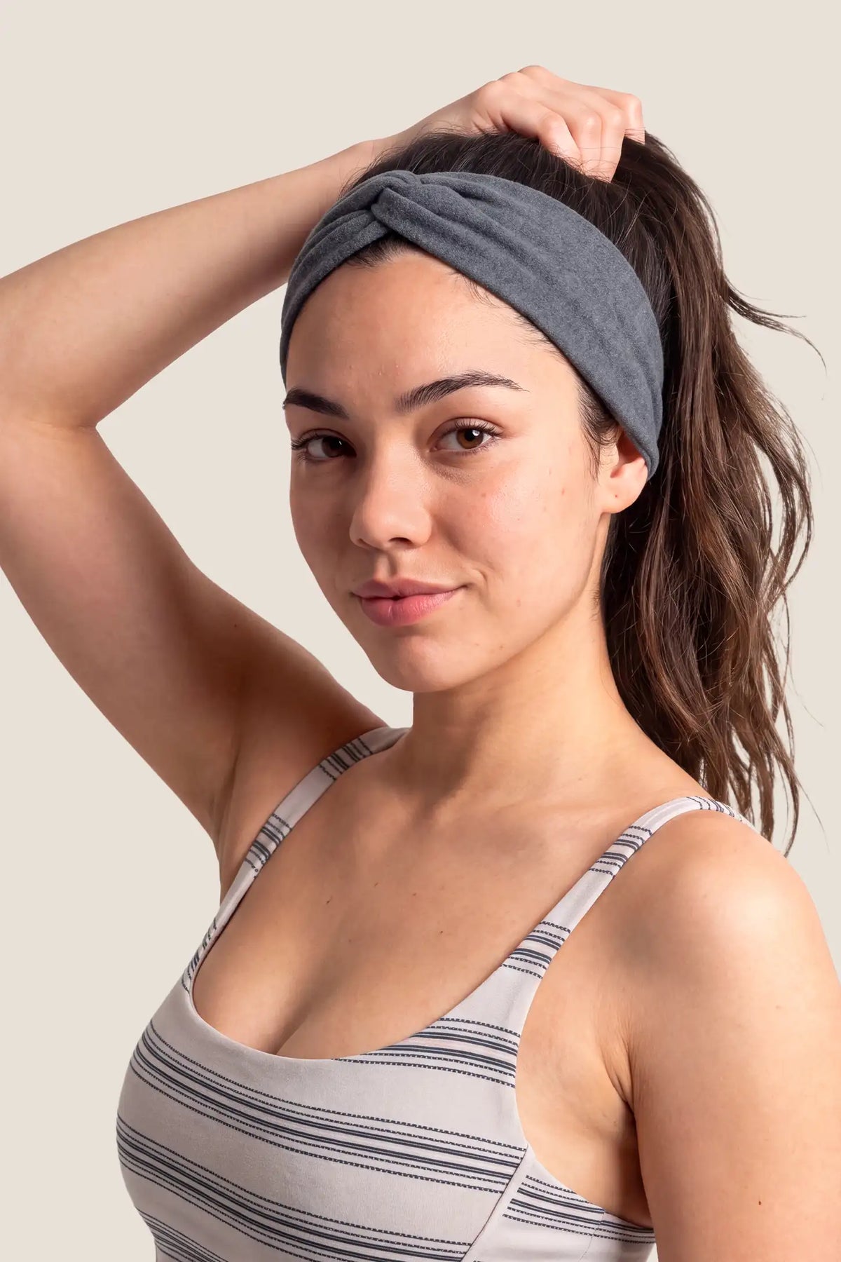 Wide Crossed Headband Wide Crossed Headband in Heather Grey featuring an overlapping front twist detail and comfortable wide fit on a smiling woman wearing a tank top, studio lifestyle portrait view.