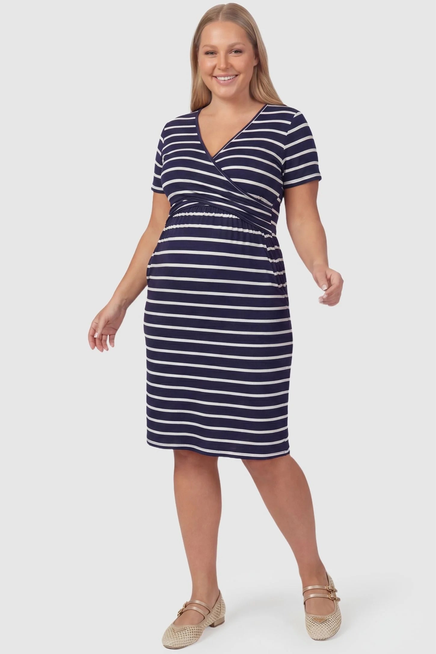 Short Sleeve Faux Wrap Maternity & Nursing Midi Dress Short Sleeve Faux Wrap Maternity & Nursing Midi Dress in navy striped print featuring V-neck faux wrap bodice and empire waist on a plus size pregnant model front view.