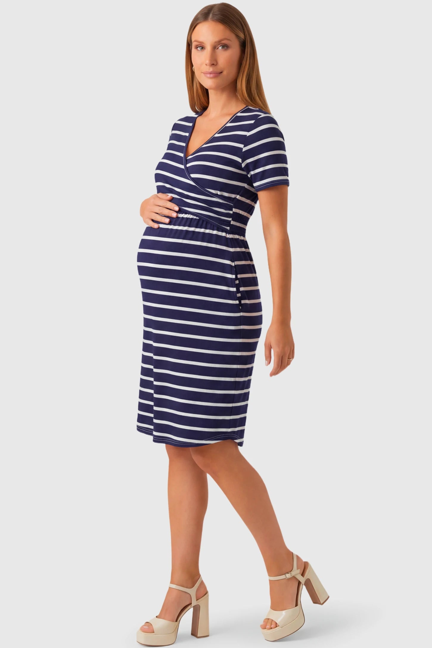 Short Sleeve Faux Wrap Maternity & Nursing Midi Dress in navy striped print featuring V-neck faux wrap bodice and empire waist on a pregnant model.