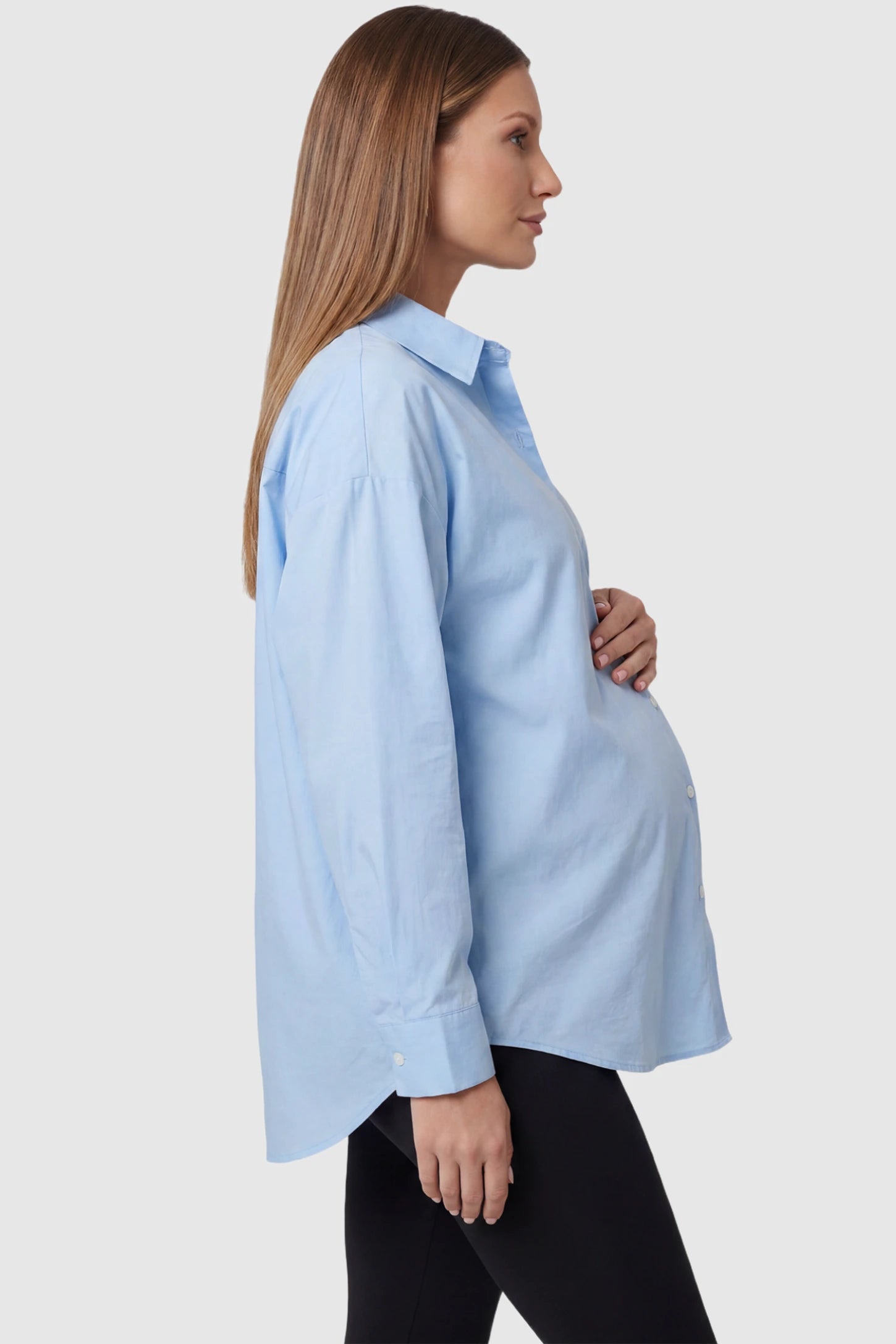 Button Down Collared Maternity Shirt in light blue featuring long sleeves and a crisp cotton finish on a pregnant model, side view.