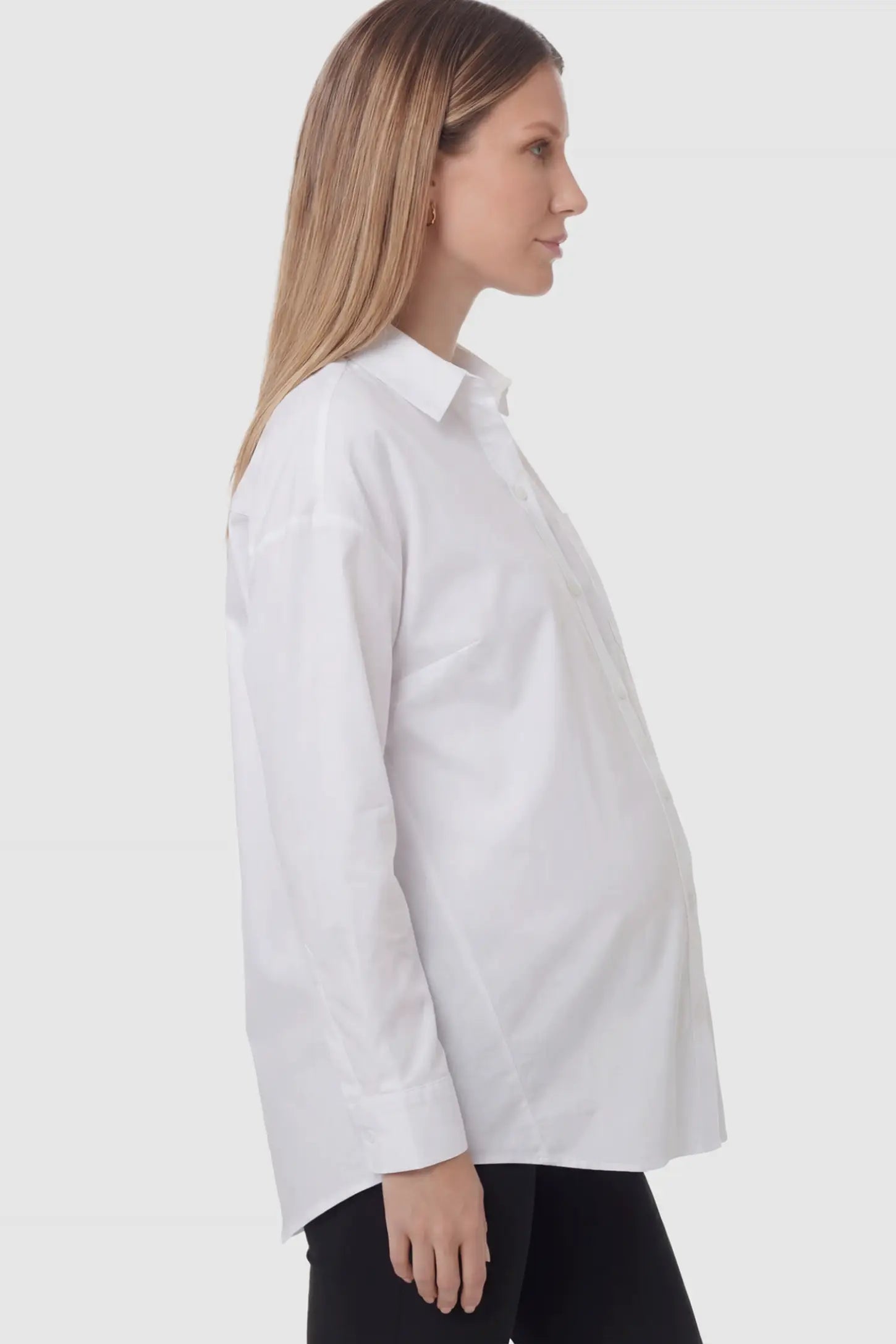 Button Down Collared Maternity Shirt Button Down Collared Maternity Shirt in white featuring long sleeves and a crisp cotton finish on a pregnant model showing side.